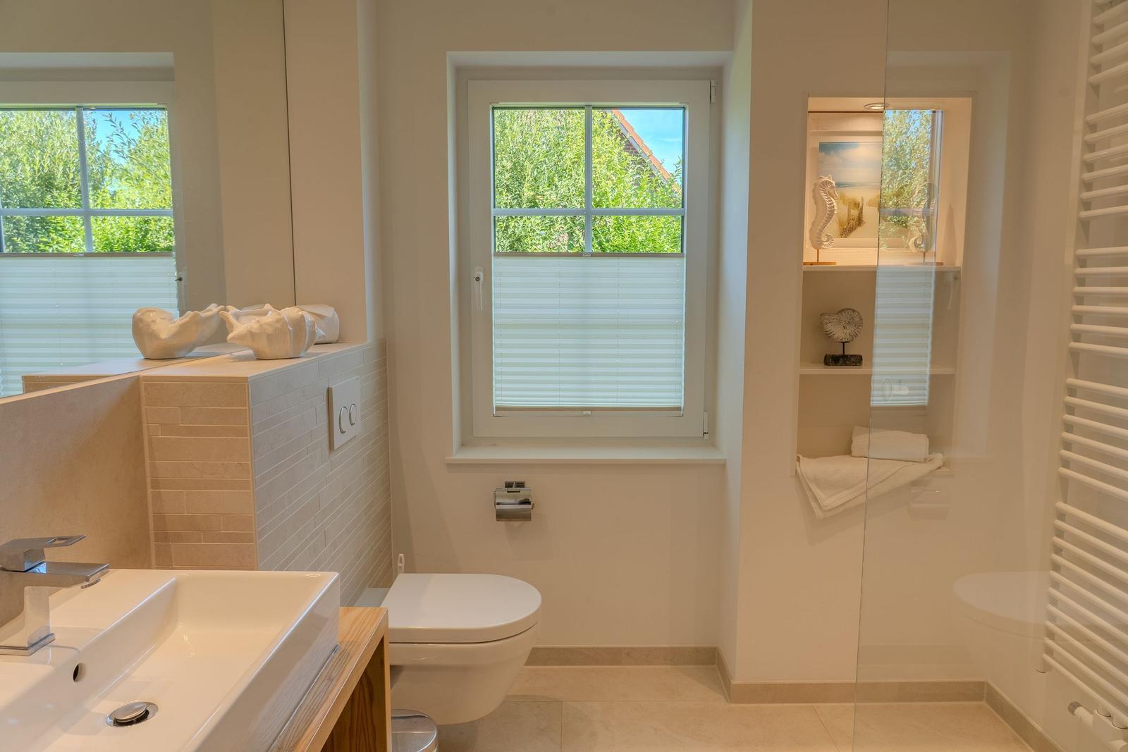 Badezimmer mit Waschbecken, Toilette und Fenster mit Blick auf Grün.