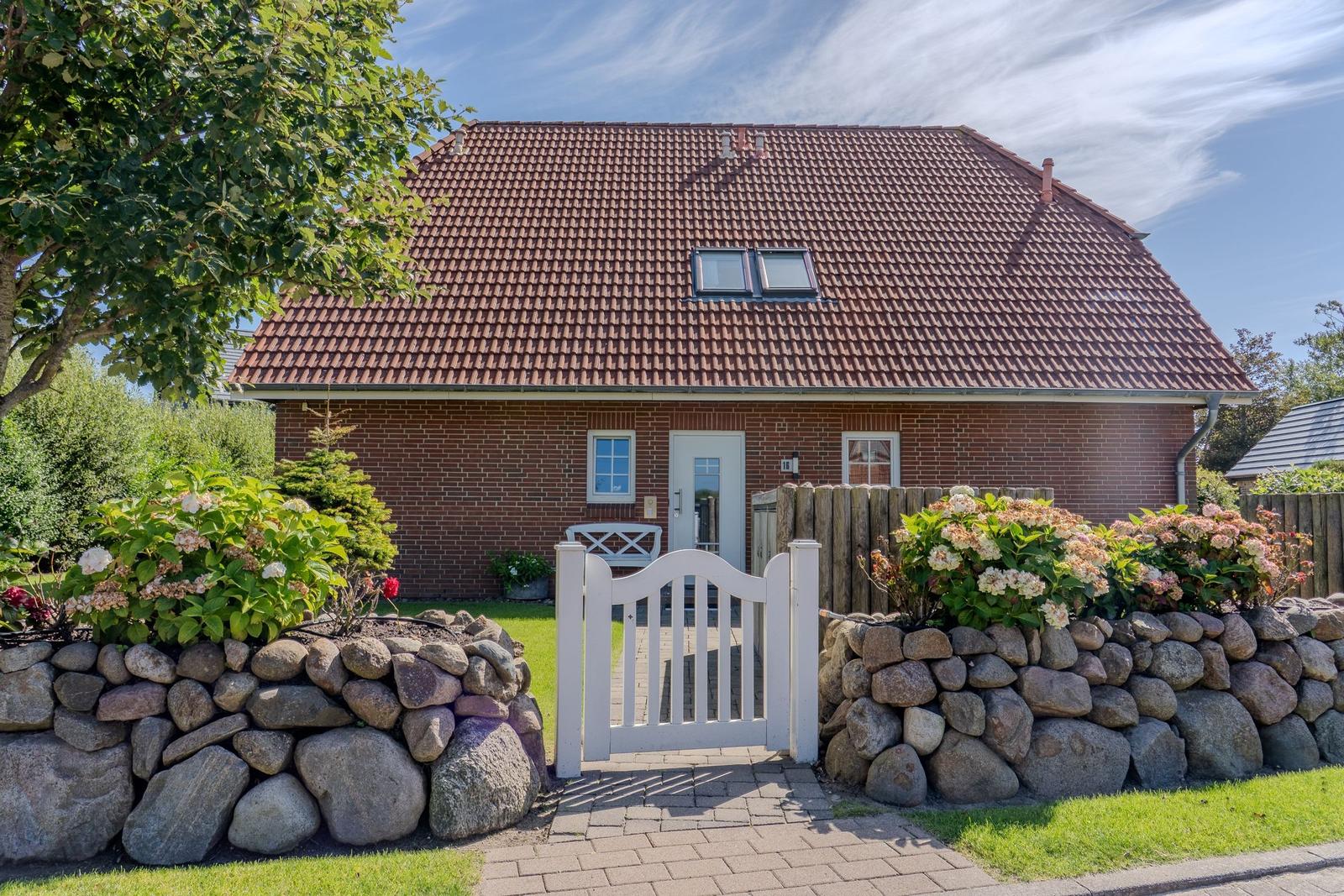 Ein Haus mit rotem Dach und Steinmauer umgeben von Blumen.