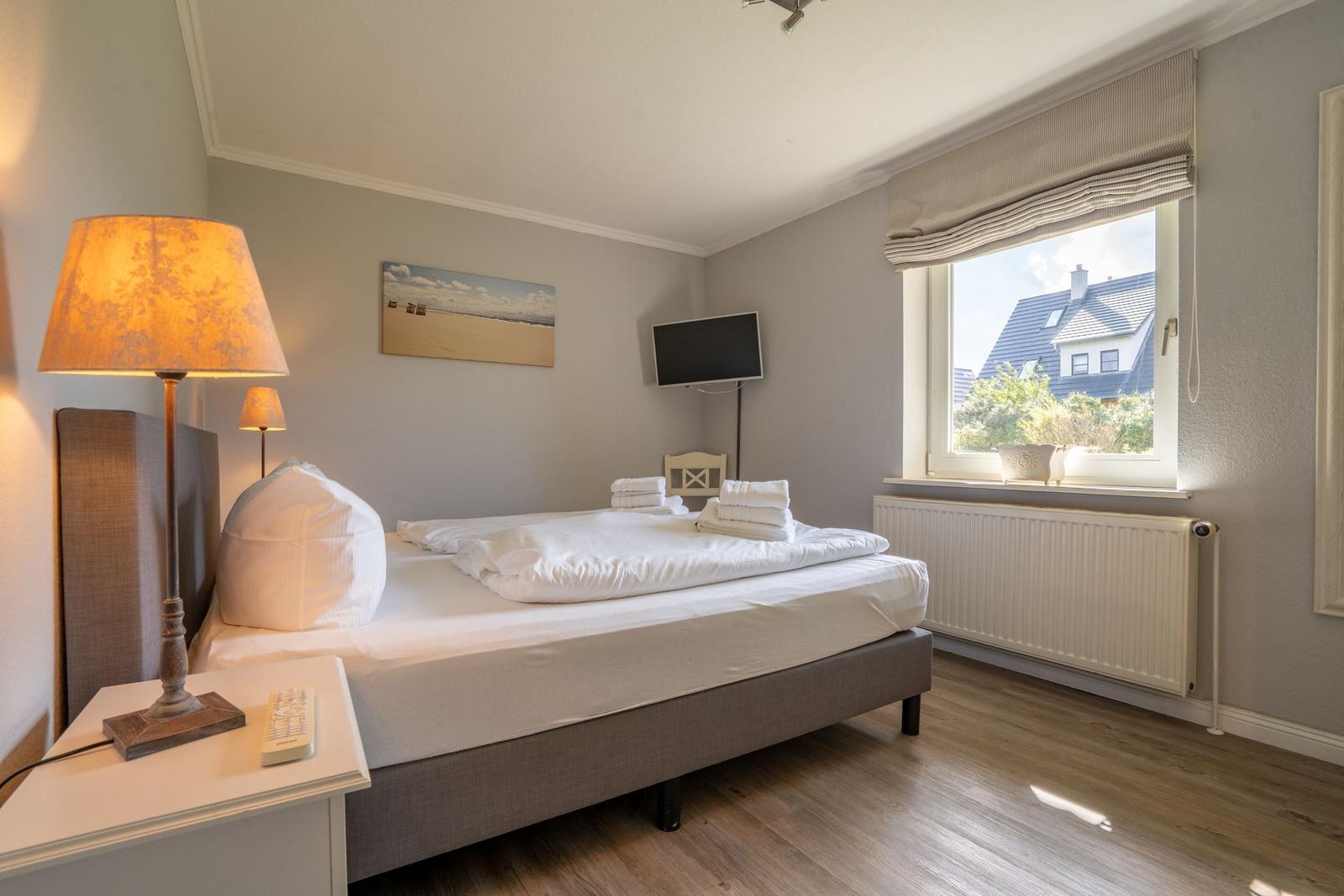 Schlafzimmer mit Bett, Fernseher und Fensterblick.