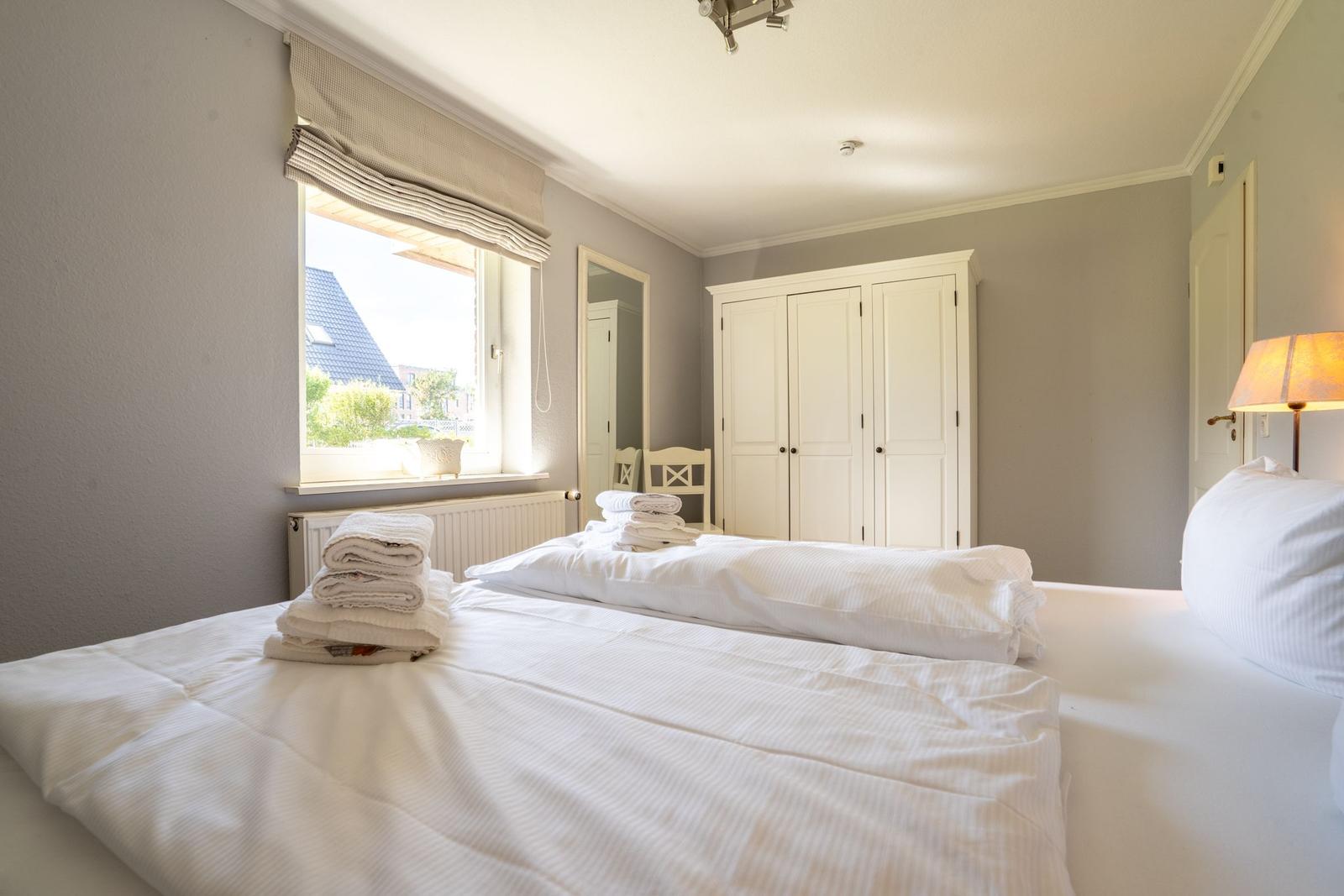 Schlafzimmer mit weißem Bett, Kleiderregal und Fensterblick
