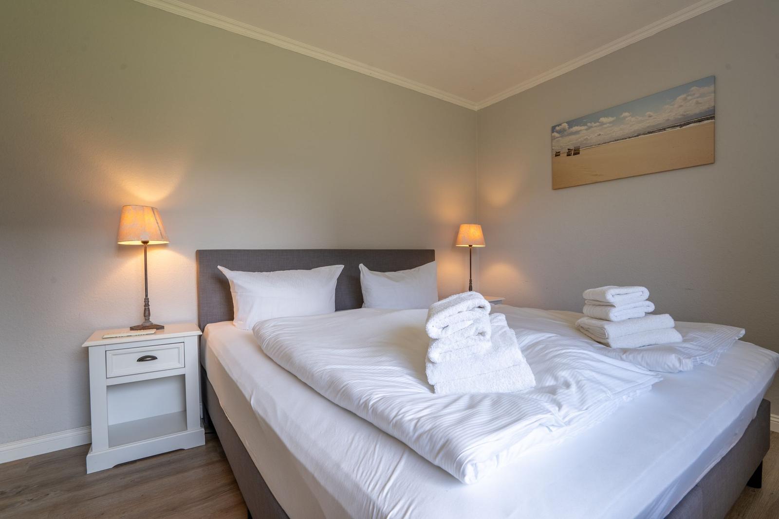 Schlafzimmer mit Bett, Nachttisch und Wandbild.