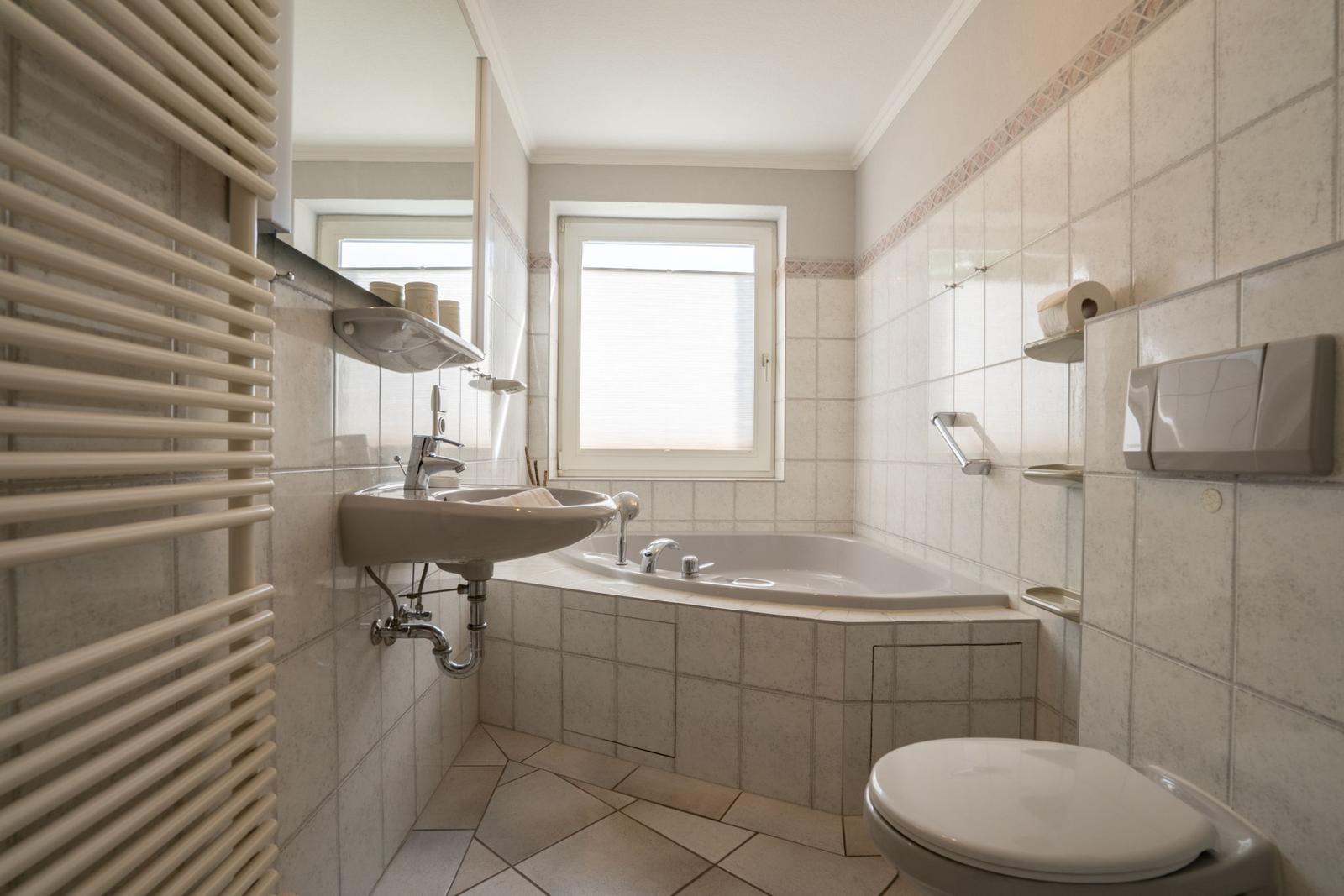 Badezimmer mit Badewanne, Waschbecken und Toilette. Fliesenwand und Fenster sichtbar.