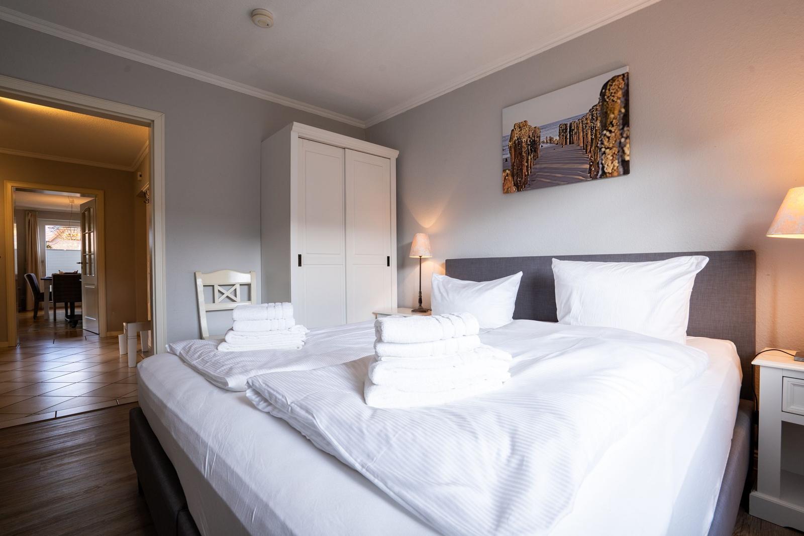 Schlafzimmer mit Bett, Kleiderkabinett und Wandbild. Blick in angrenzende Räume.