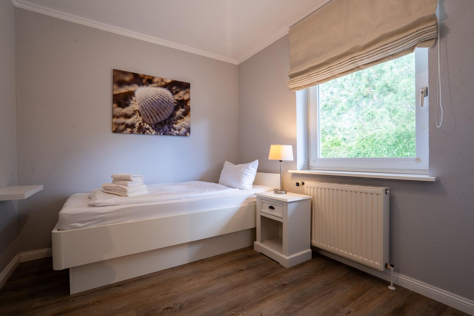 Ein Schlafzimmer mit Bett, Nachttisch und Fenster mit Blick auf Bäume.