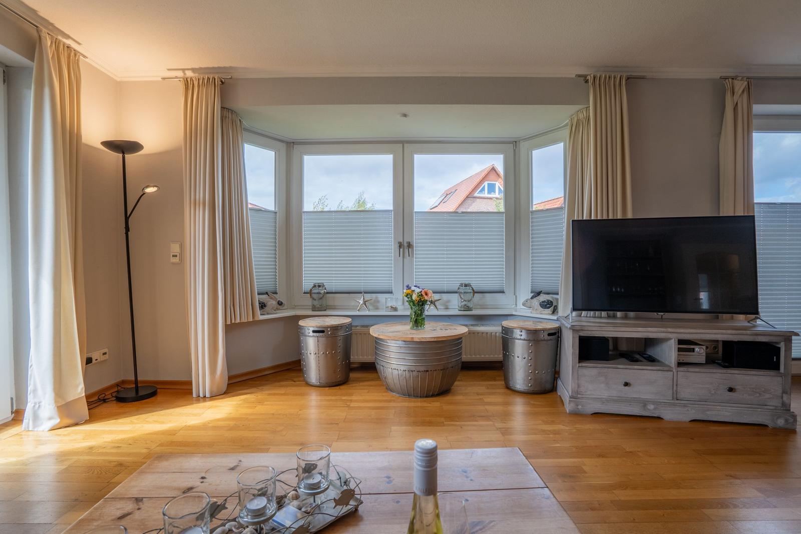 Wohnzimmer mit Holzboden, TV, Fenster und Tischen.
