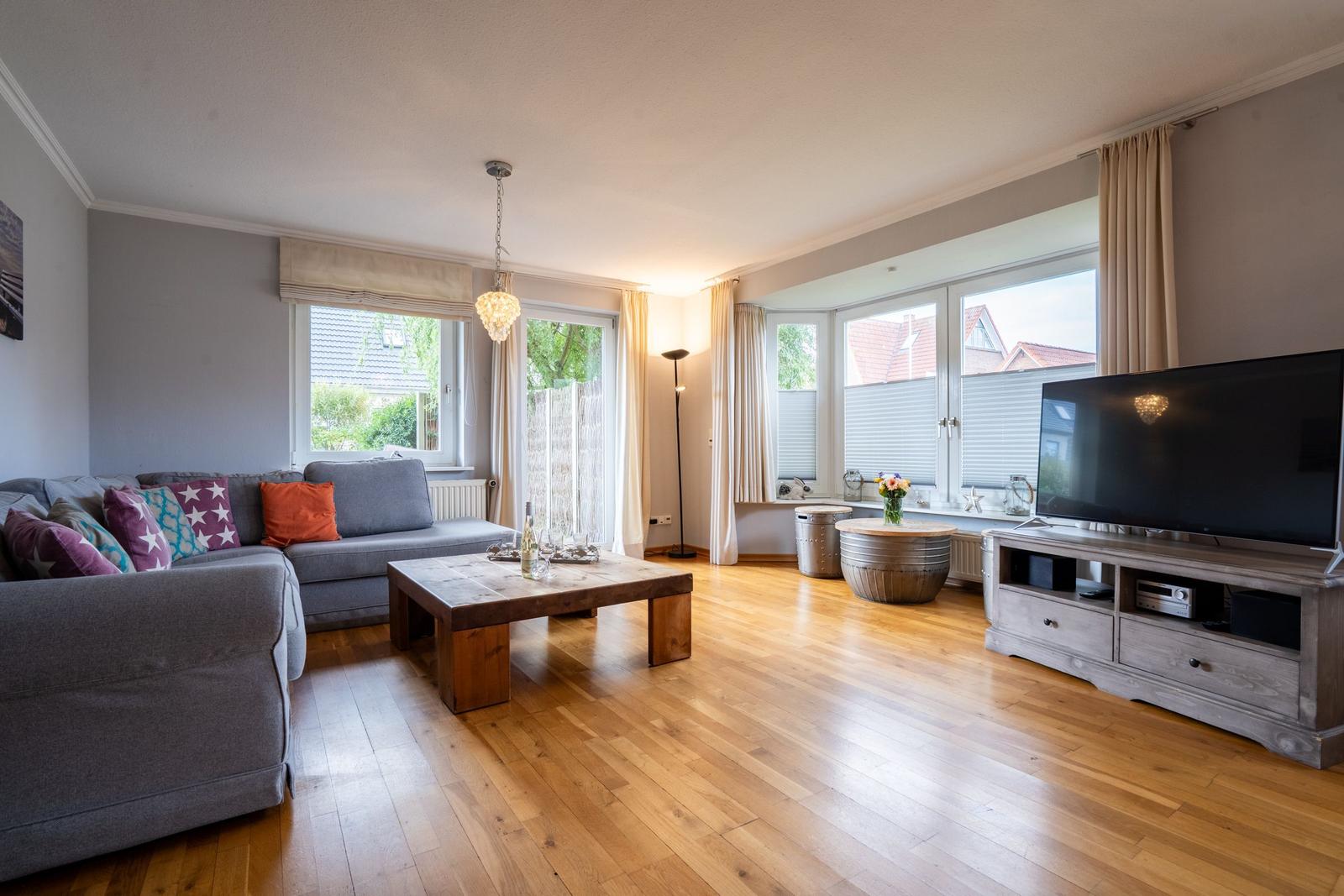 Wohnzimmer mit Sofa, Holztisch und TV. Holzfußboden und große Fenster.