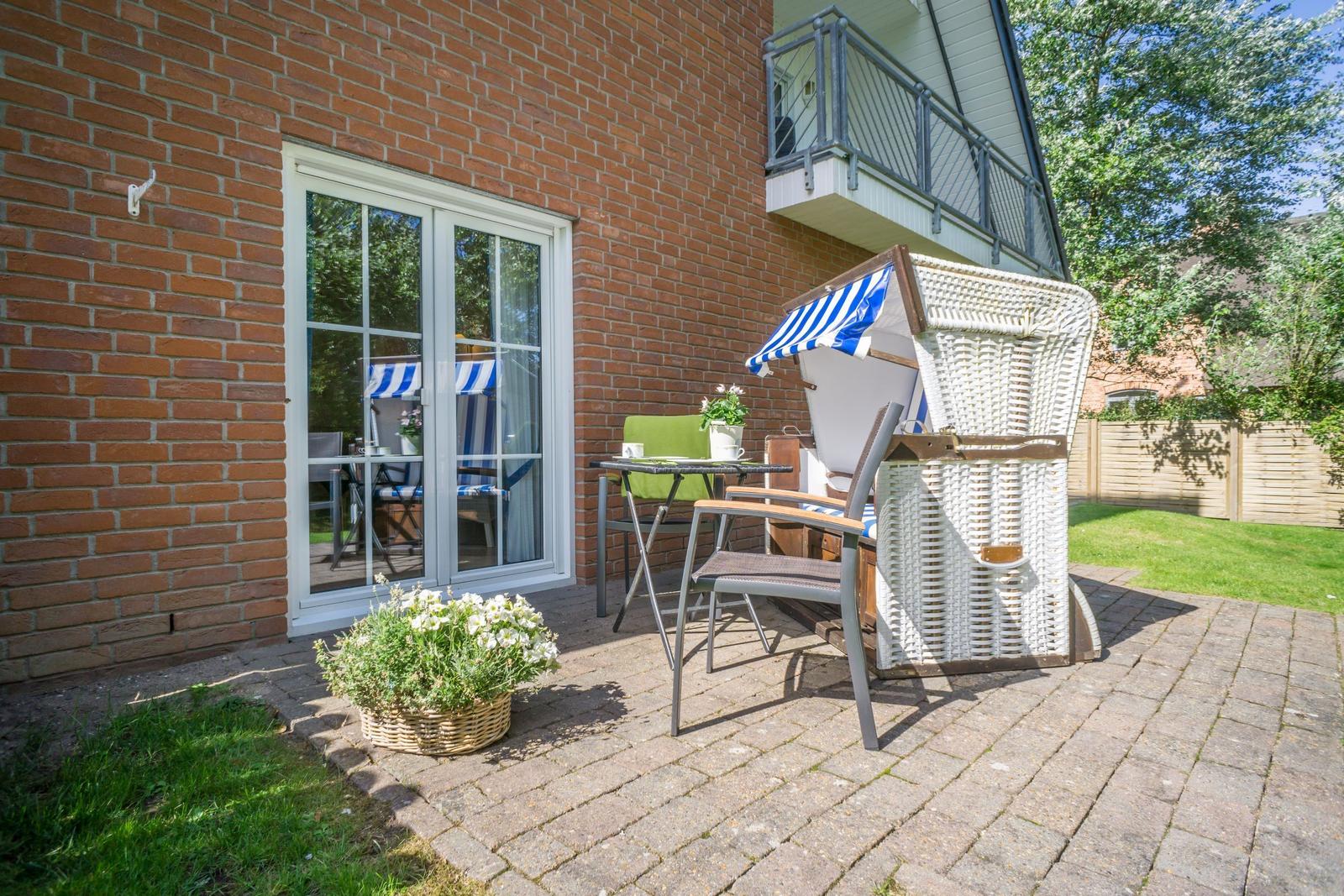 Terrasse mit Liegestuhl, Tisch und Blumen vor Backsteinhaus.