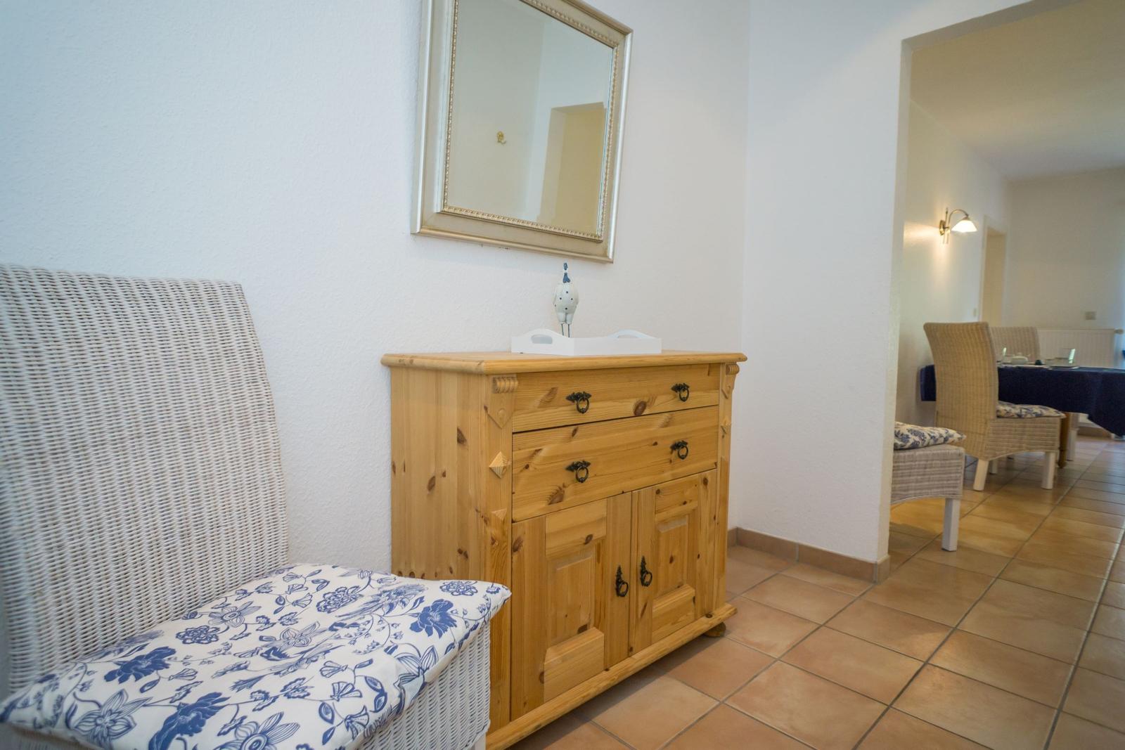 Holzschrank mit Spiegel, weiße Rattanbank mit blau-weißem Kissen.