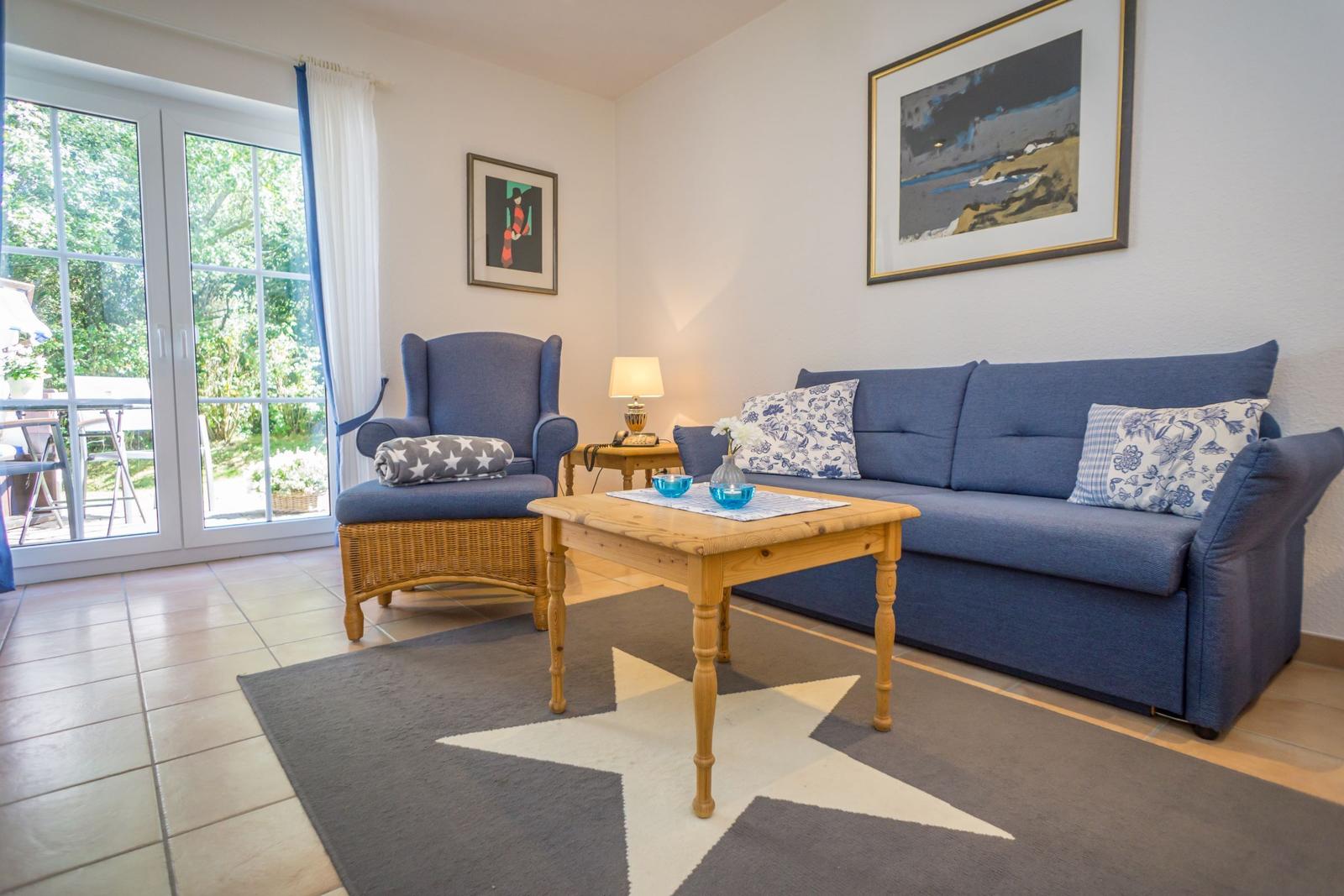 Wohnzimmer mit blauem Sofa, Holztisch und Blick auf den Garten.