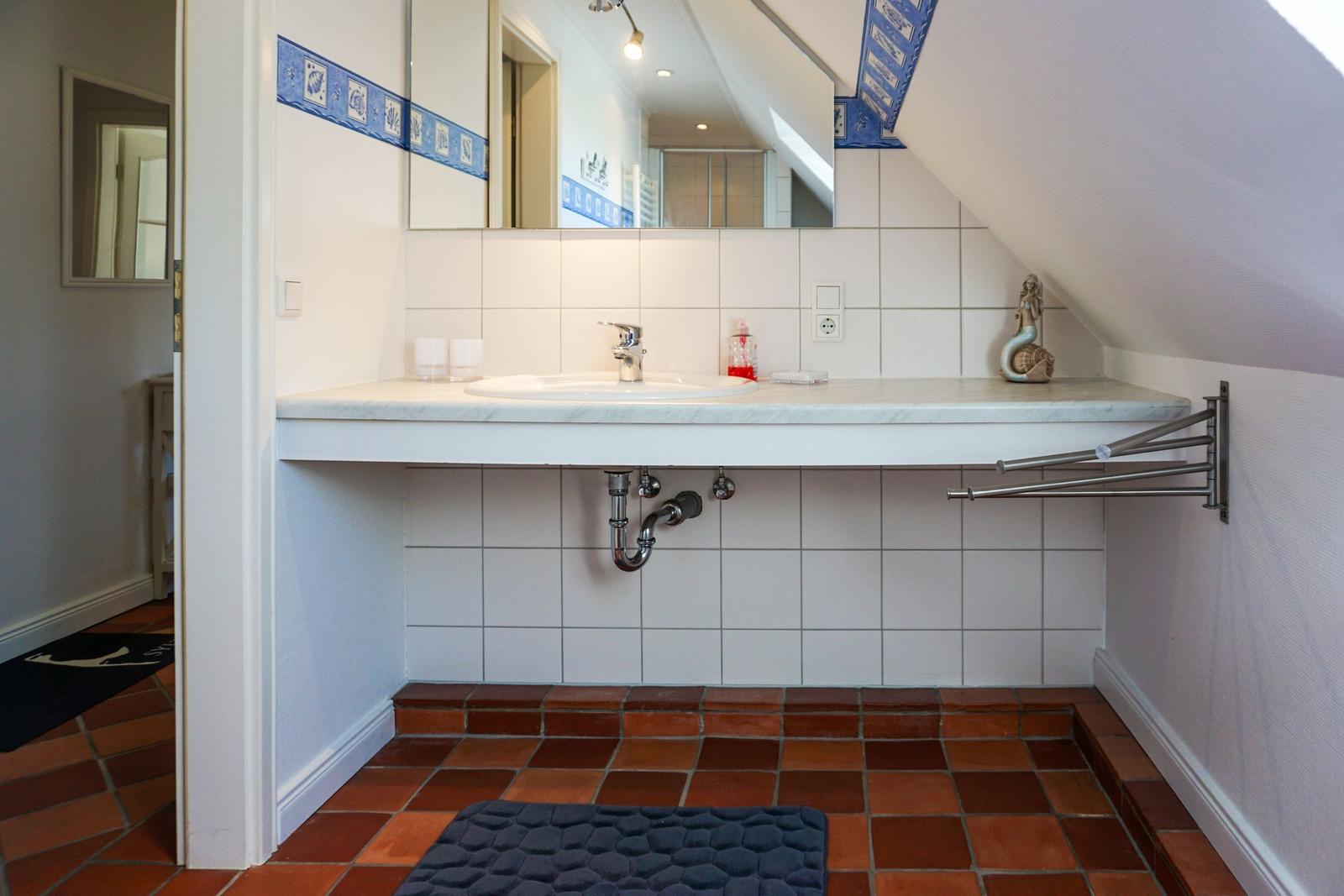 Badezimmer mit Waschbecken, Spiegel und Terrakottboden
