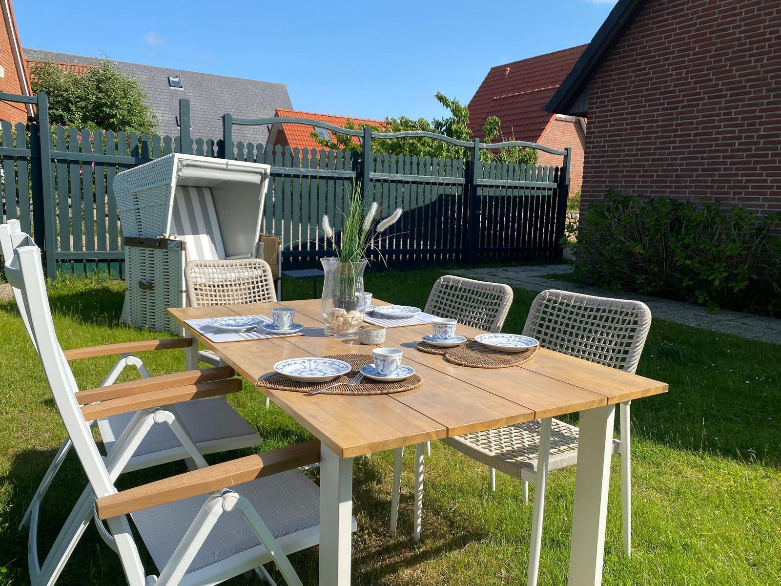 Hinterhof mit Tisch, Stühlen und Strandkorb. Grünfläche und Zaun im Hintergrund.