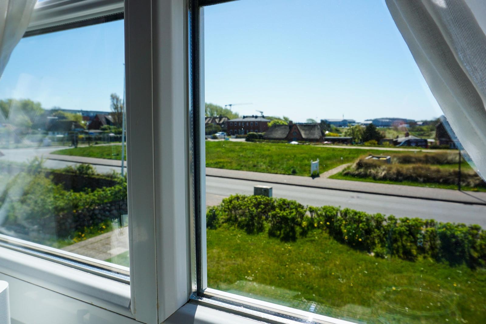 Durch das Fenster blickt man auf eine grüne Wiese und Straßen im Dorf.