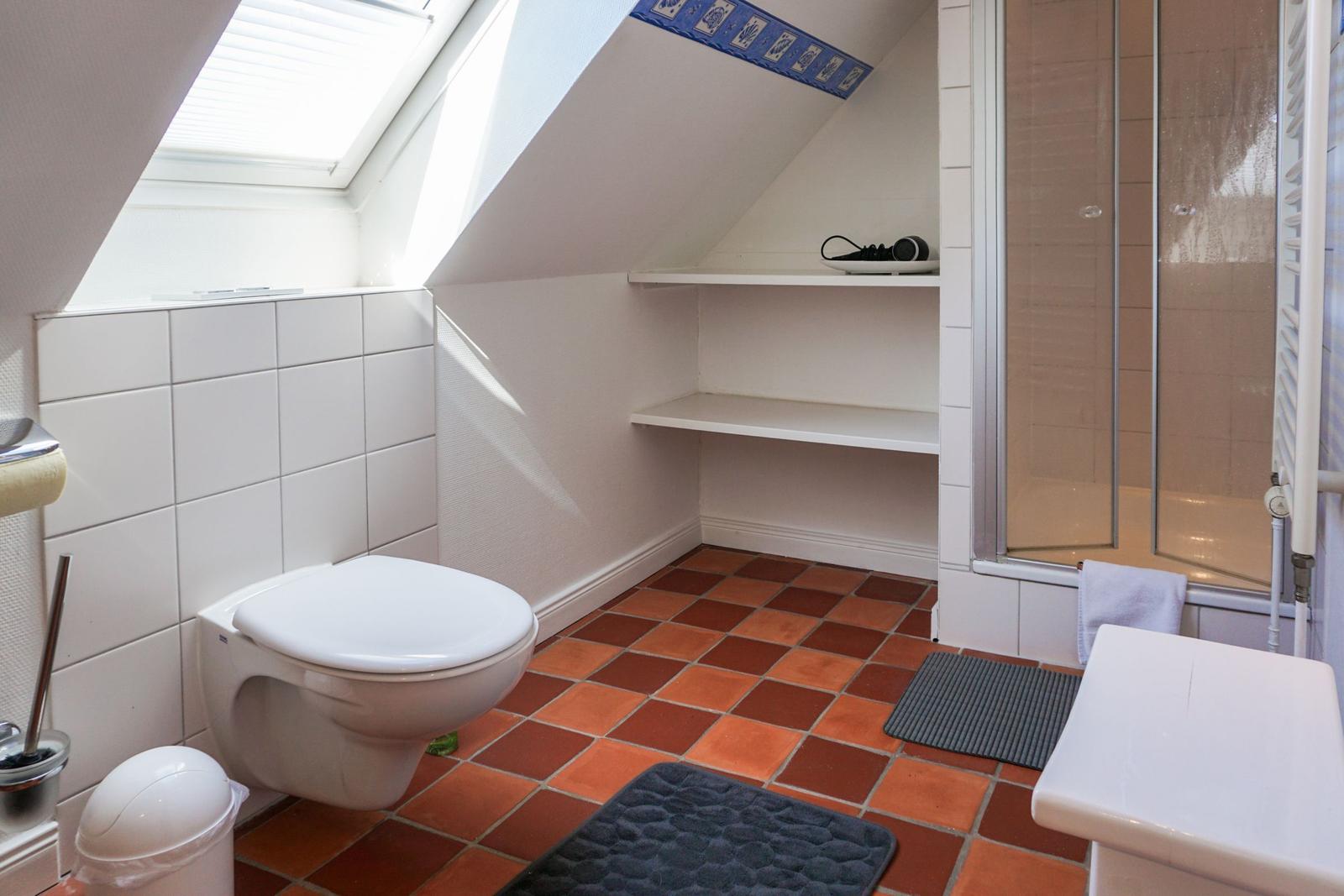 Badezimmer mit Dusche, Toilette und Waschbecken unter Dachschräge.