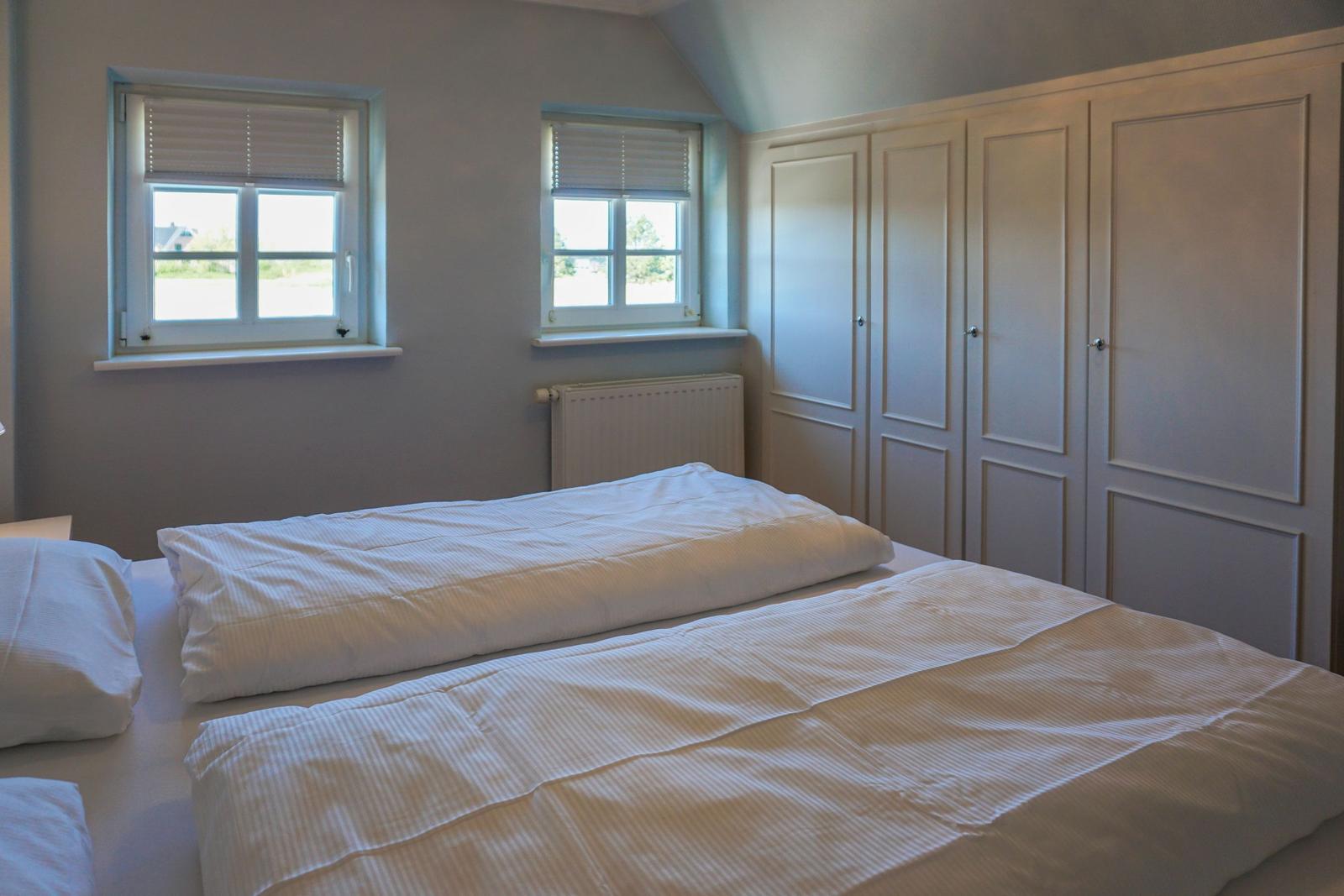 Schlafzimmer mit Doppelbett, zwei Fenstern und Kleiderschrank.