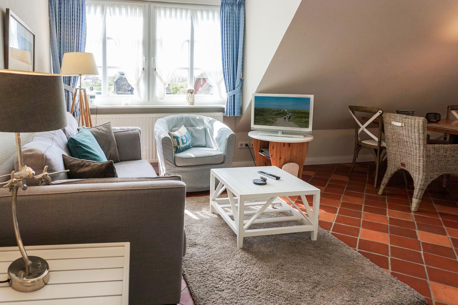 Wohnzimmer mit Sofa, Sessel, Fernseher und Esstisch.
