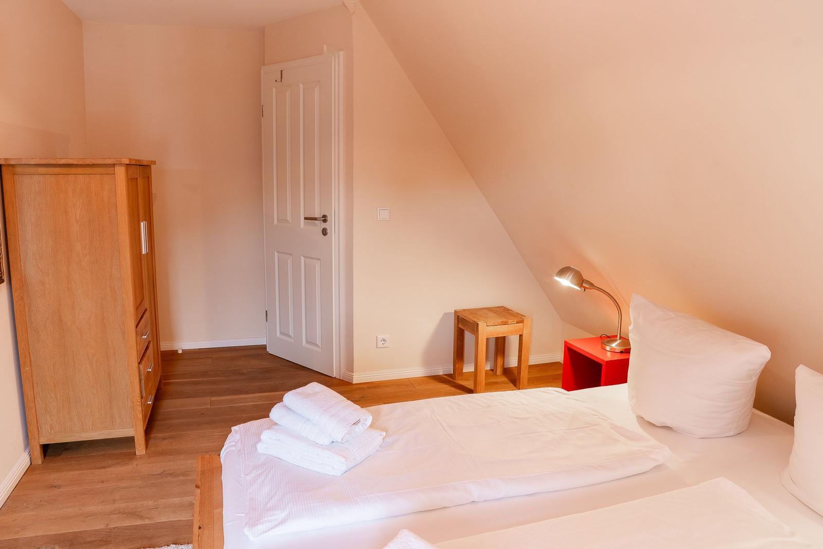 Bedroom with bed, wardrobe, and nightstand. Attic slope and wooden floor.