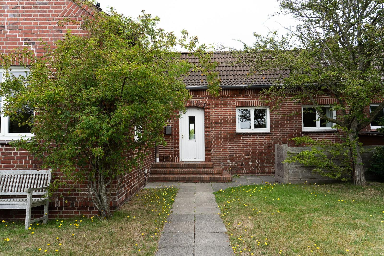 Red brick house with white door and paved walkway.