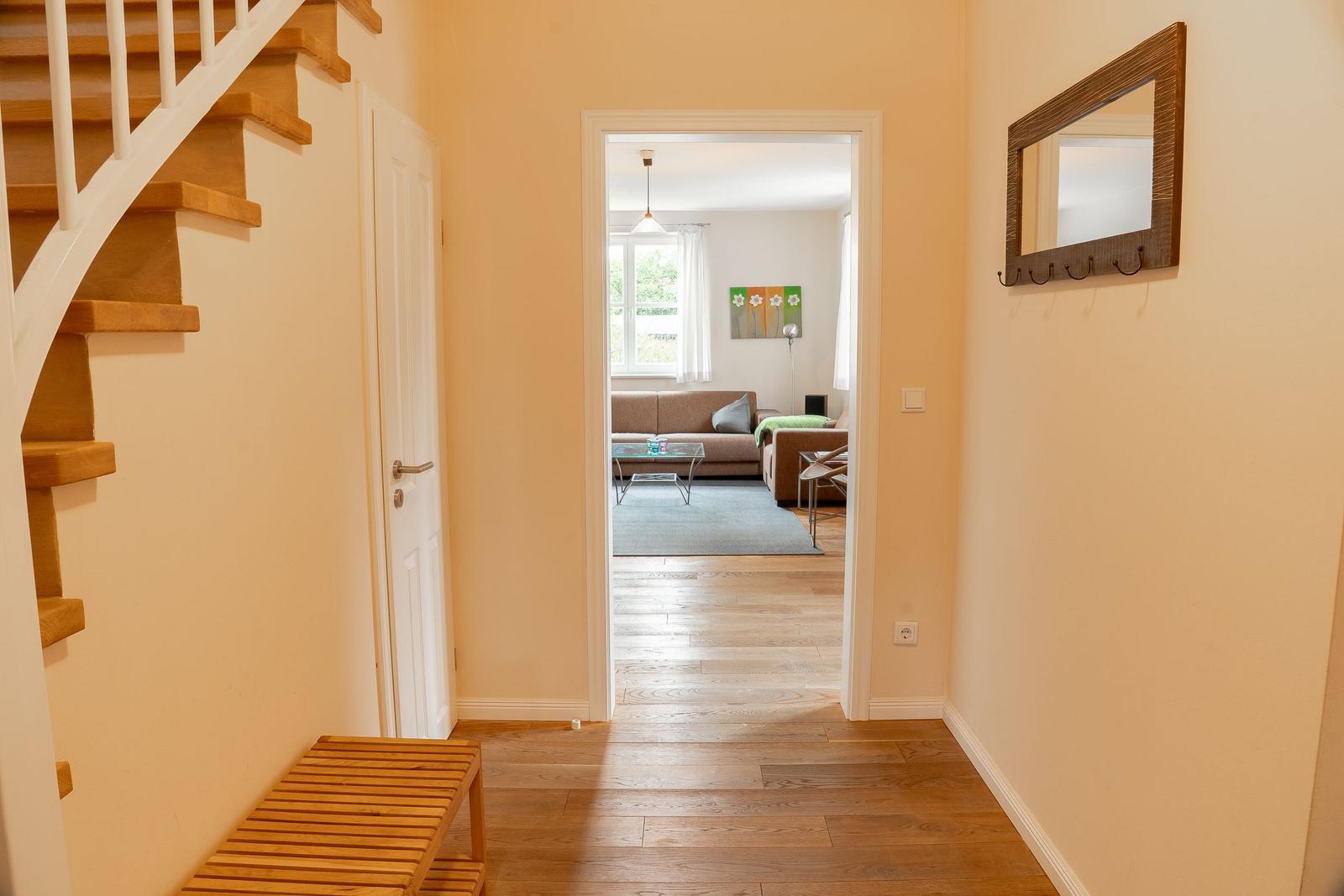Hallway with wooden staircase and view into living room with sofa and window.