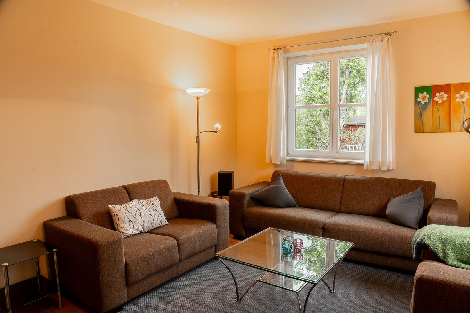 Living room with two sofas, glass table, and window with view of trees.