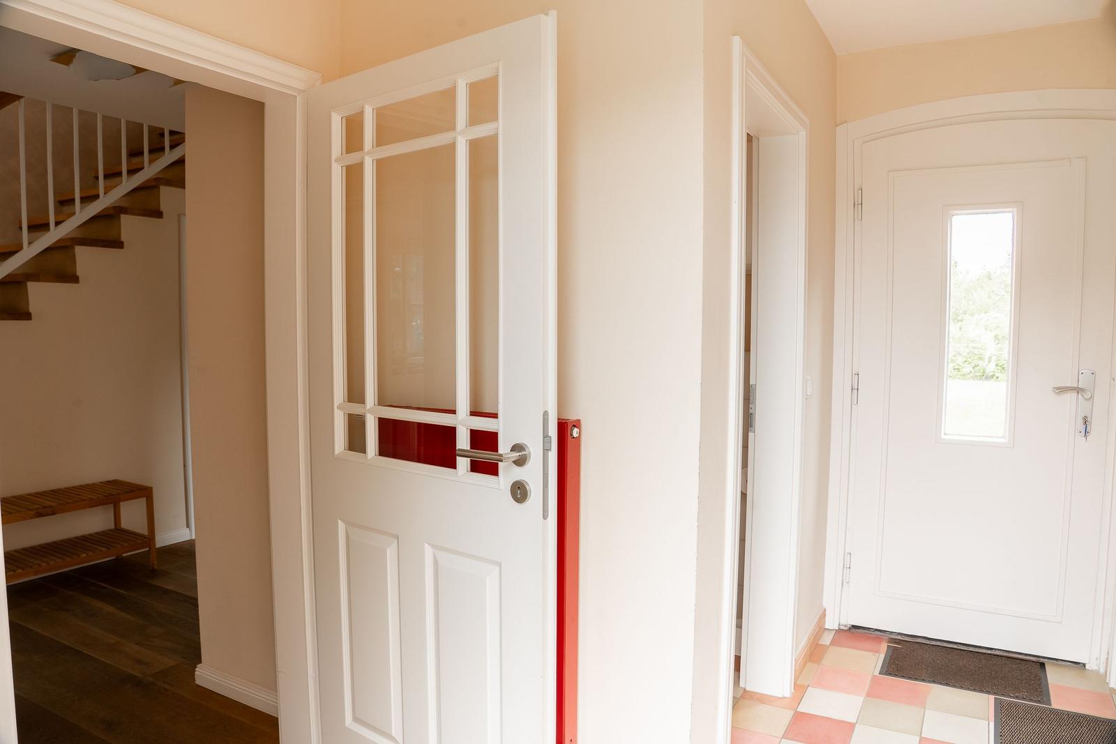 Entrance area with white doors and tiled floor. Staircase left, main door right.
