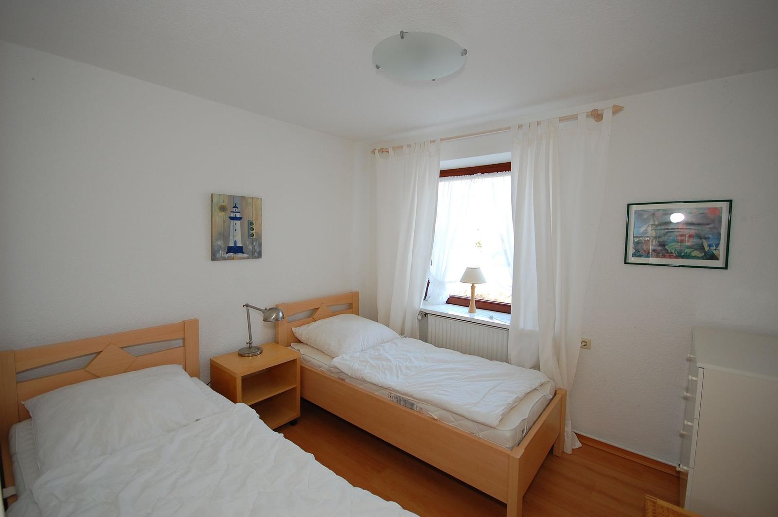 Two beds, window with curtains, nightstand, and pictures on the walls.
