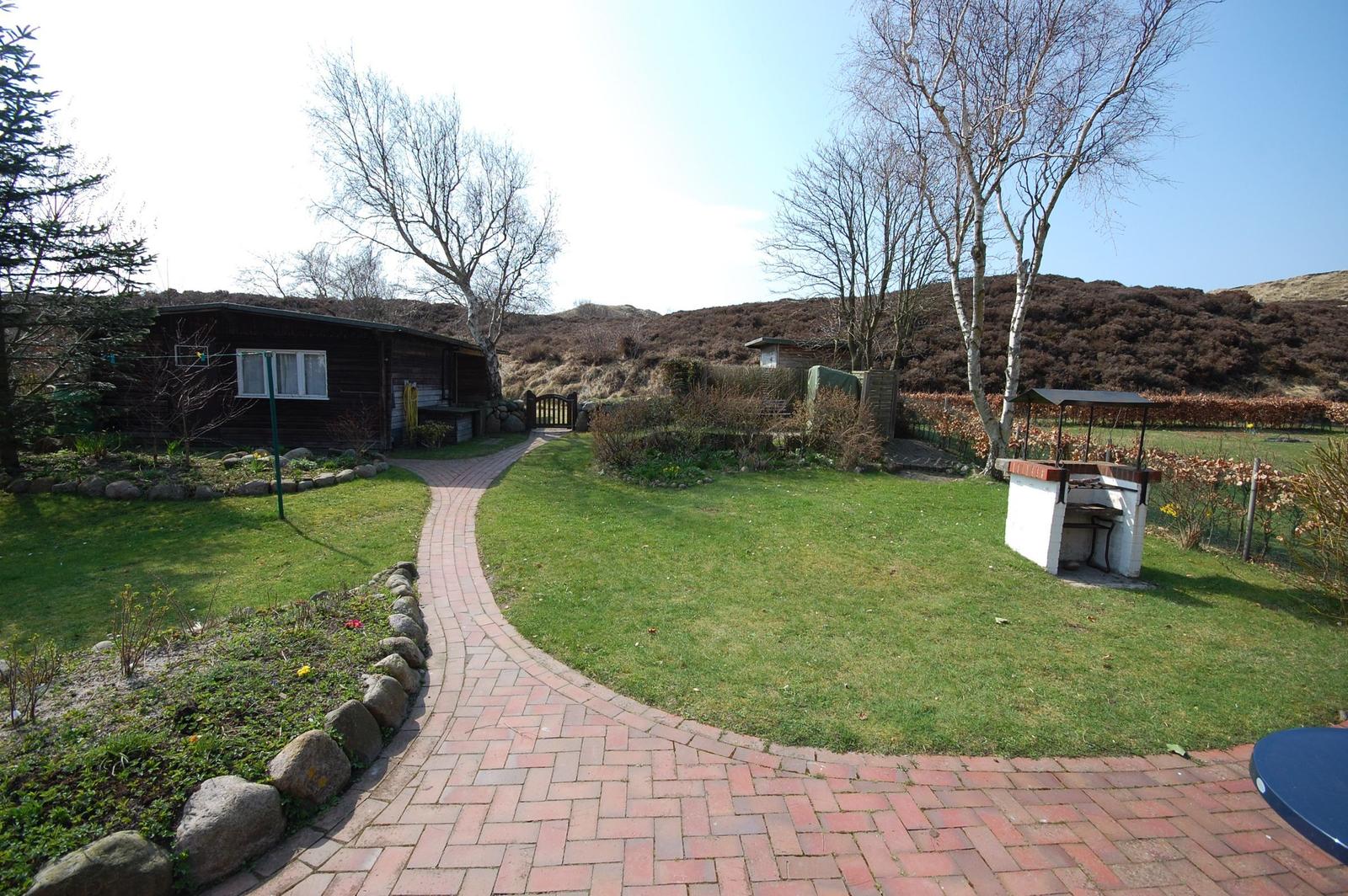House with garden, stone path, and grill. Background: hills with trees.