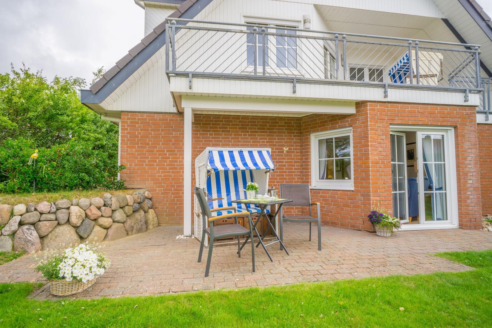 Terrace with lounge furniture and flowers in front of a house with balcony.