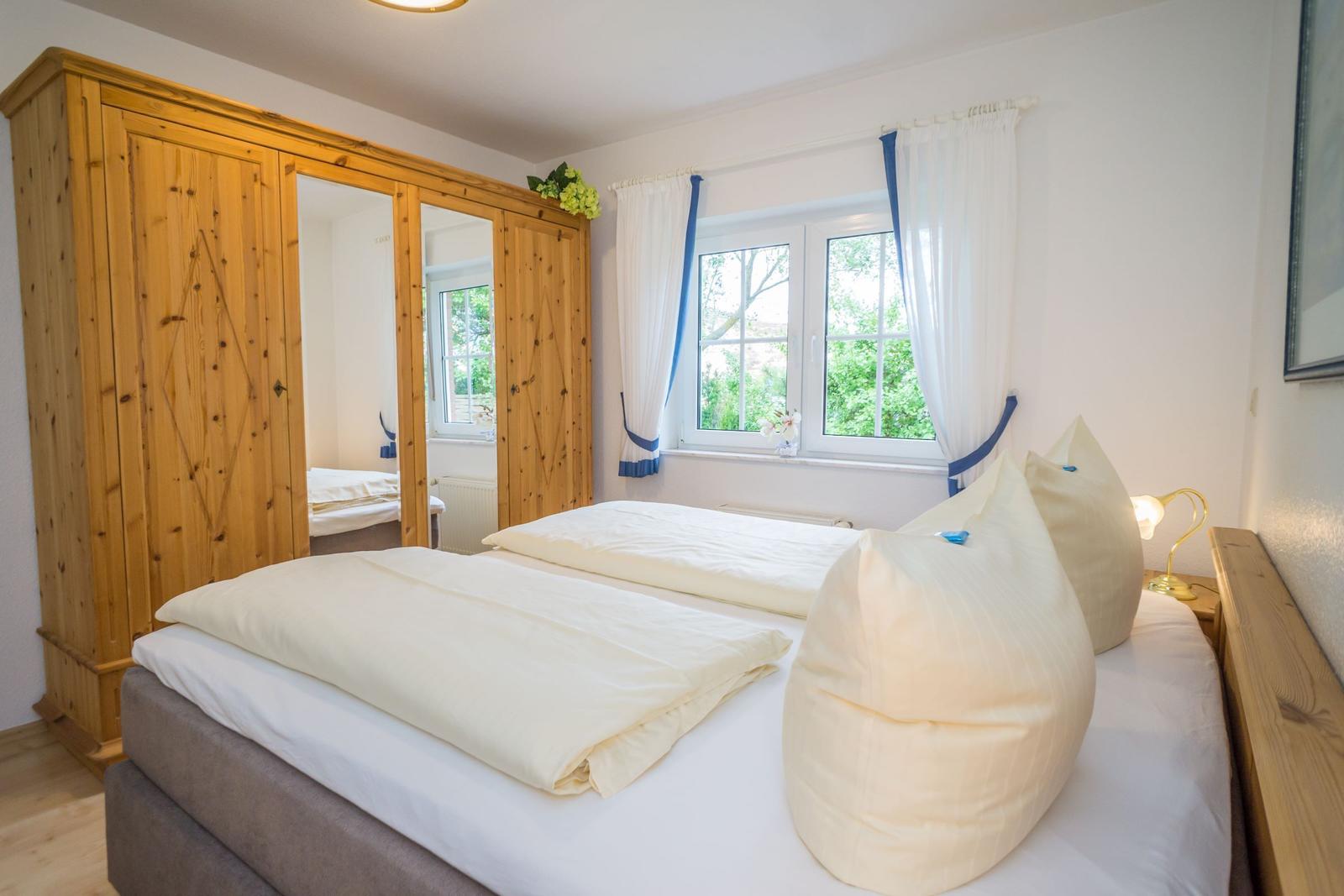 Bedroom with double bed, wooden wardrobe, and window with view of greenery.