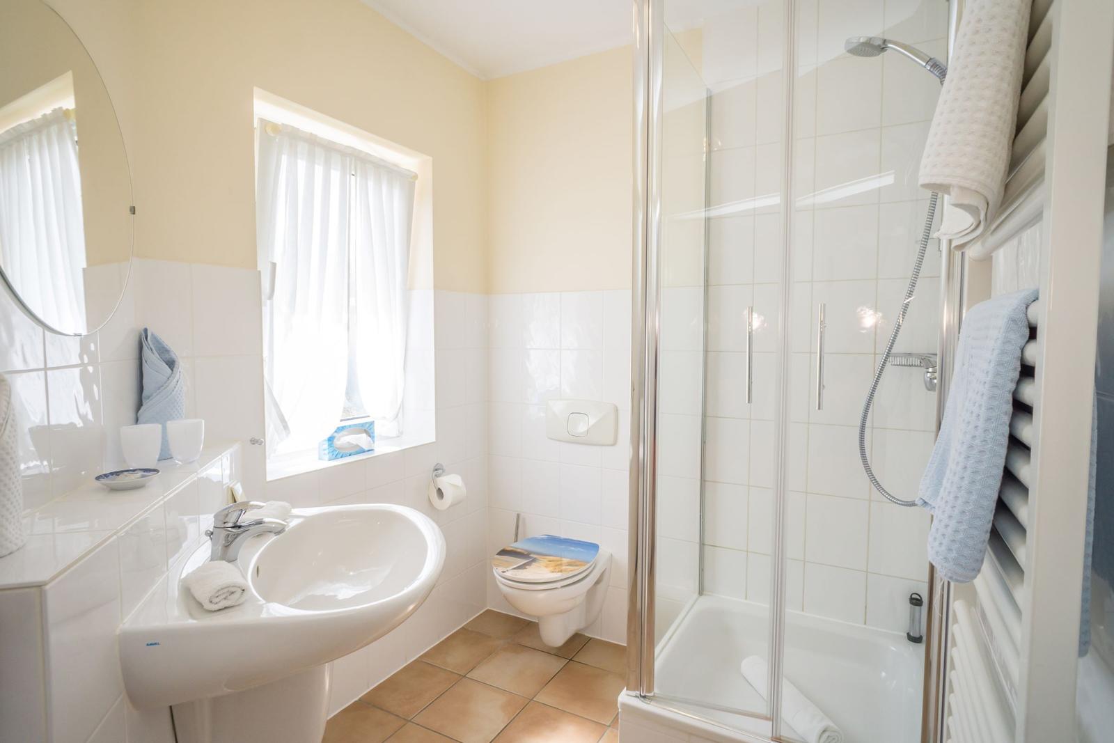 Bathroom with shower, sink, and toilet. Window with white curtains.