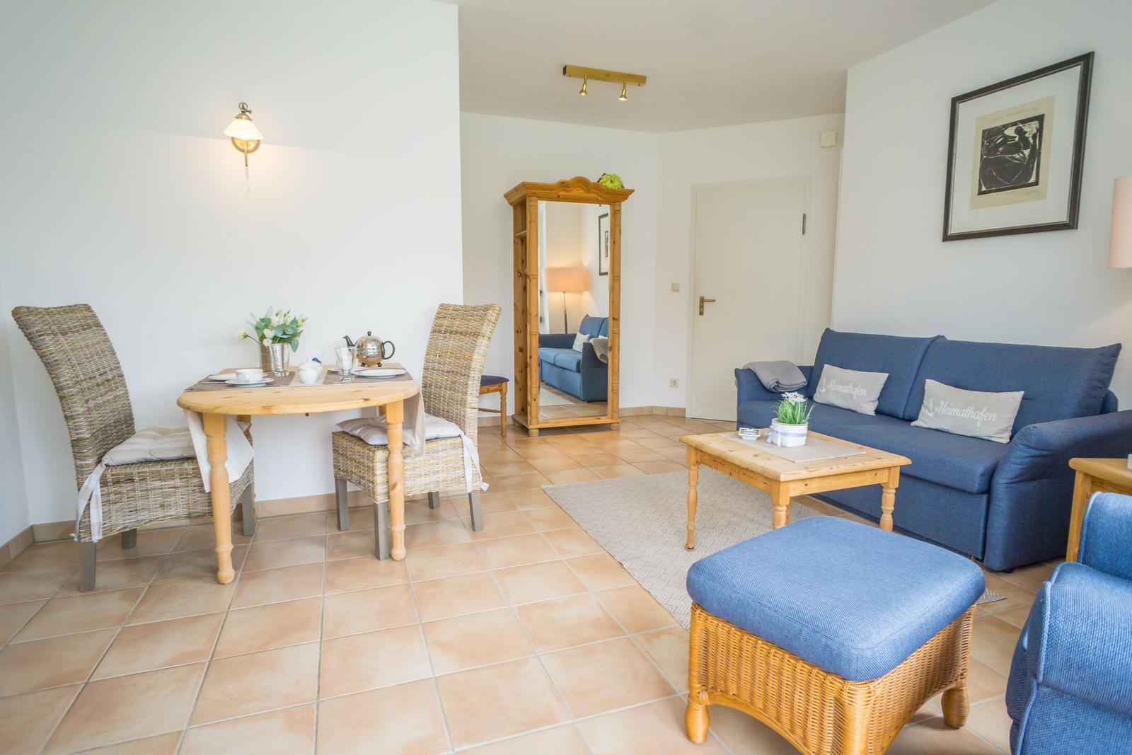 Living and dining area with blue sofa, wooden table and chairs, mirror and teapot.