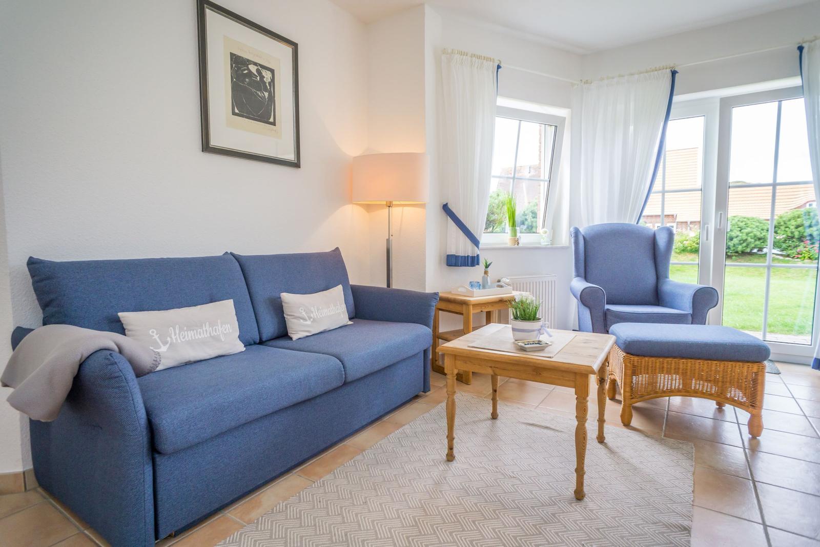 Blue sofa with cushions, armchair and table in living room with garden view.