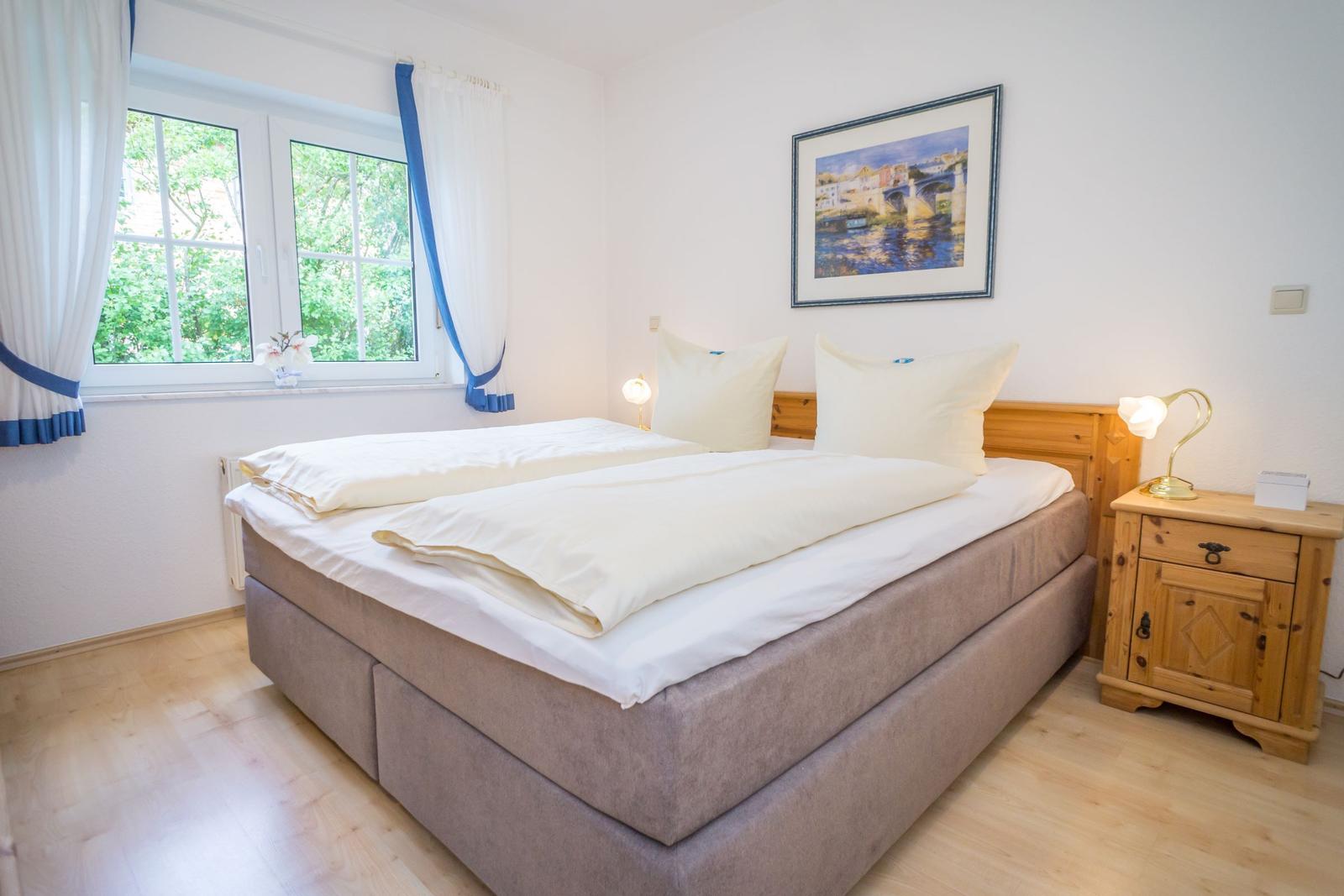 Bedroom with double bed, wooden cabinet, and window with view of greenery.