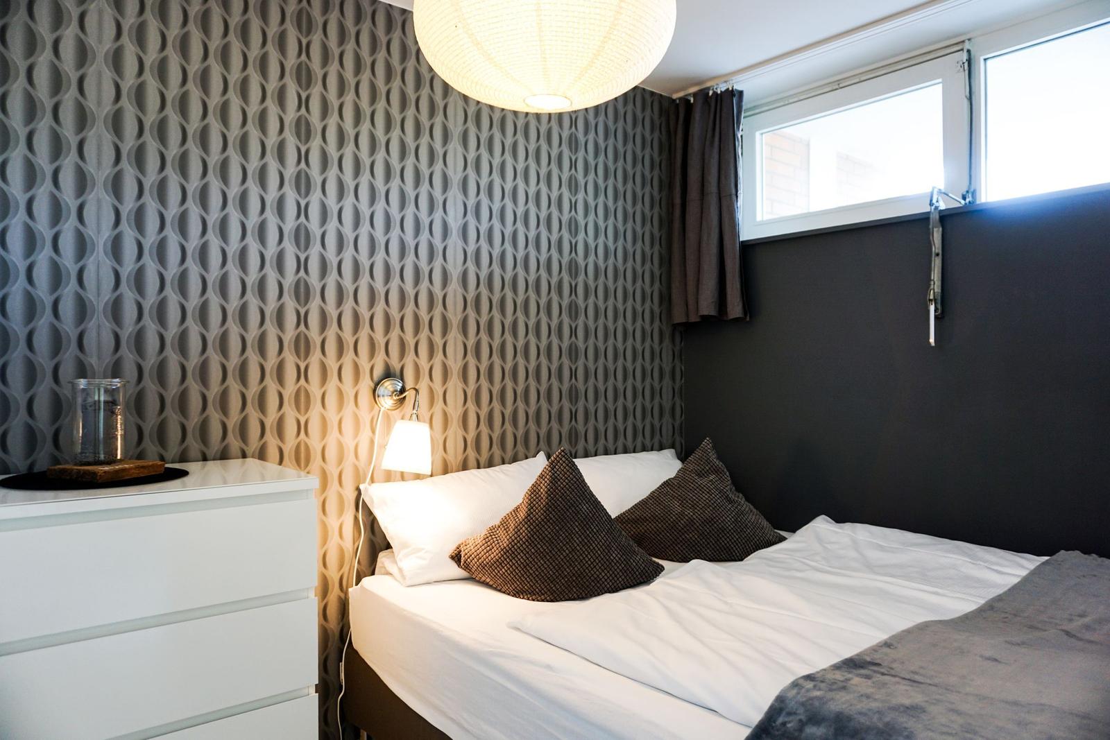 Schlafzimmer mit Bett, Nachttisch und Wandbeleuchtung.