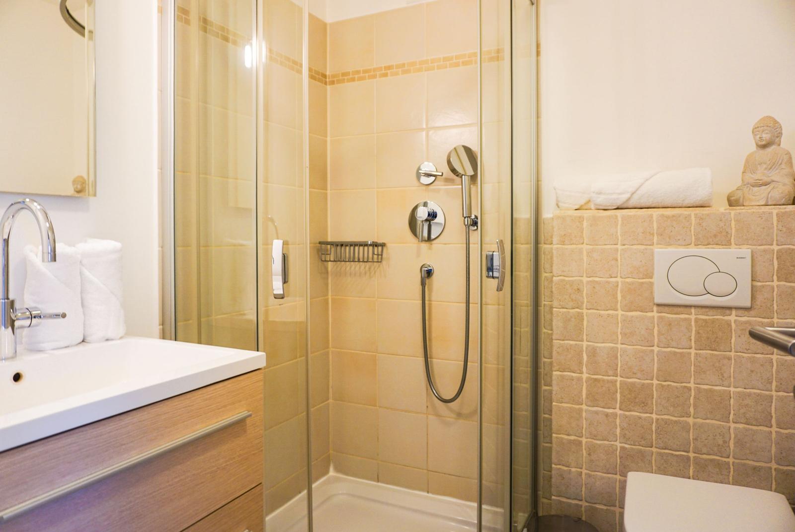 Bad mit Dusche, Waschbecken und Toilette. Fliesenwand und Spiegel sind sichtbar.