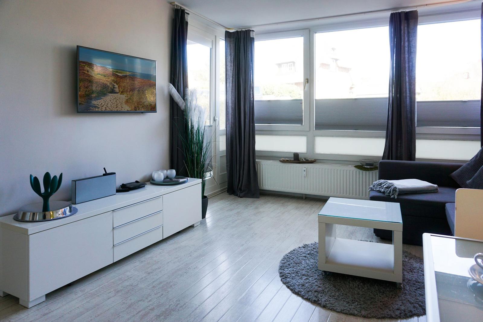 Wohnzimmer mit Sofa, Fernseher und großen Fenstern.