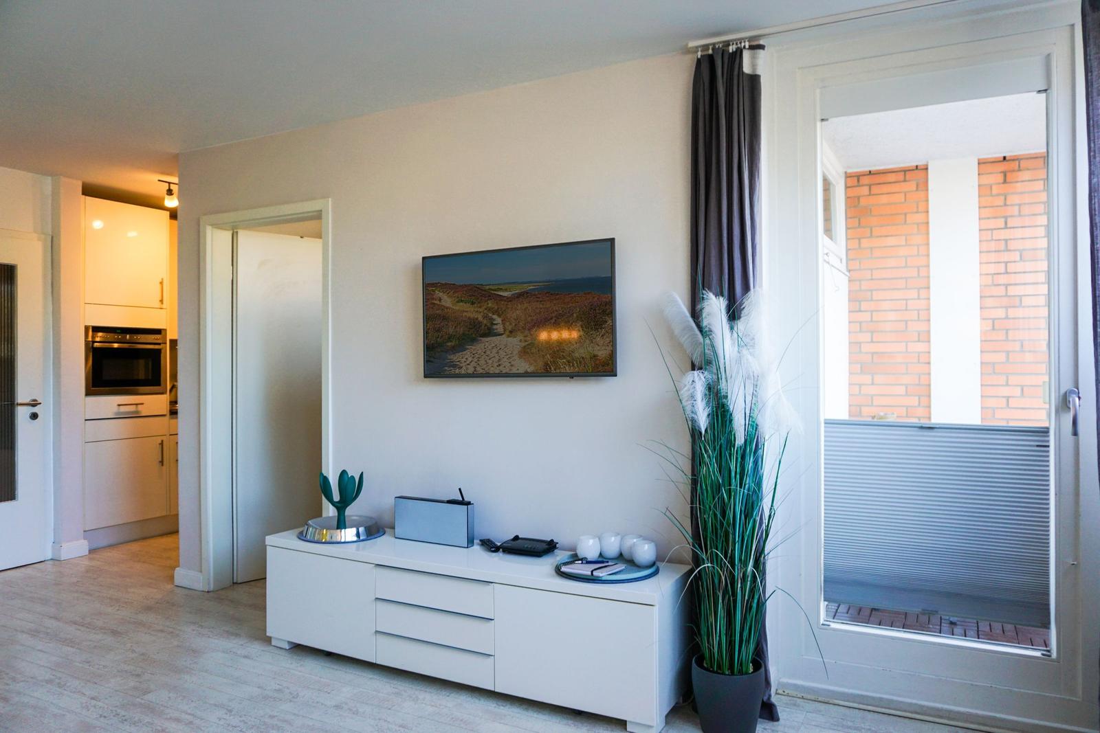 Wohnzimmer mit Fernseher, weiße Kommode und Blick auf Balkon