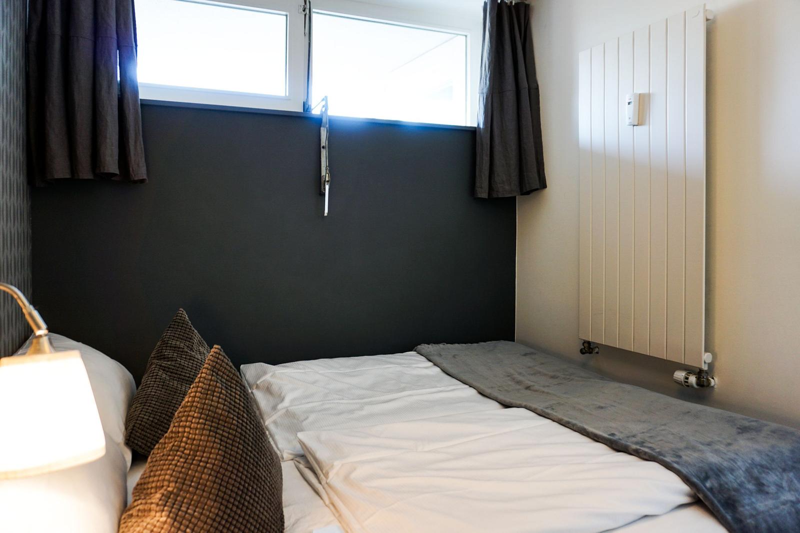 Schlafzimmer mit Bett, Fenster und Heizkörper an der Wand.