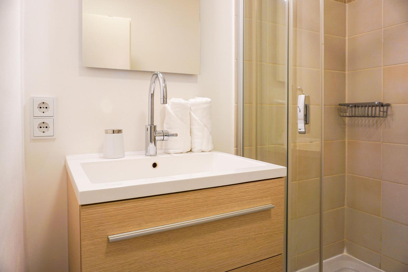 Bad mit Waschbecken, Spiegel und Dusche mit Glaswand