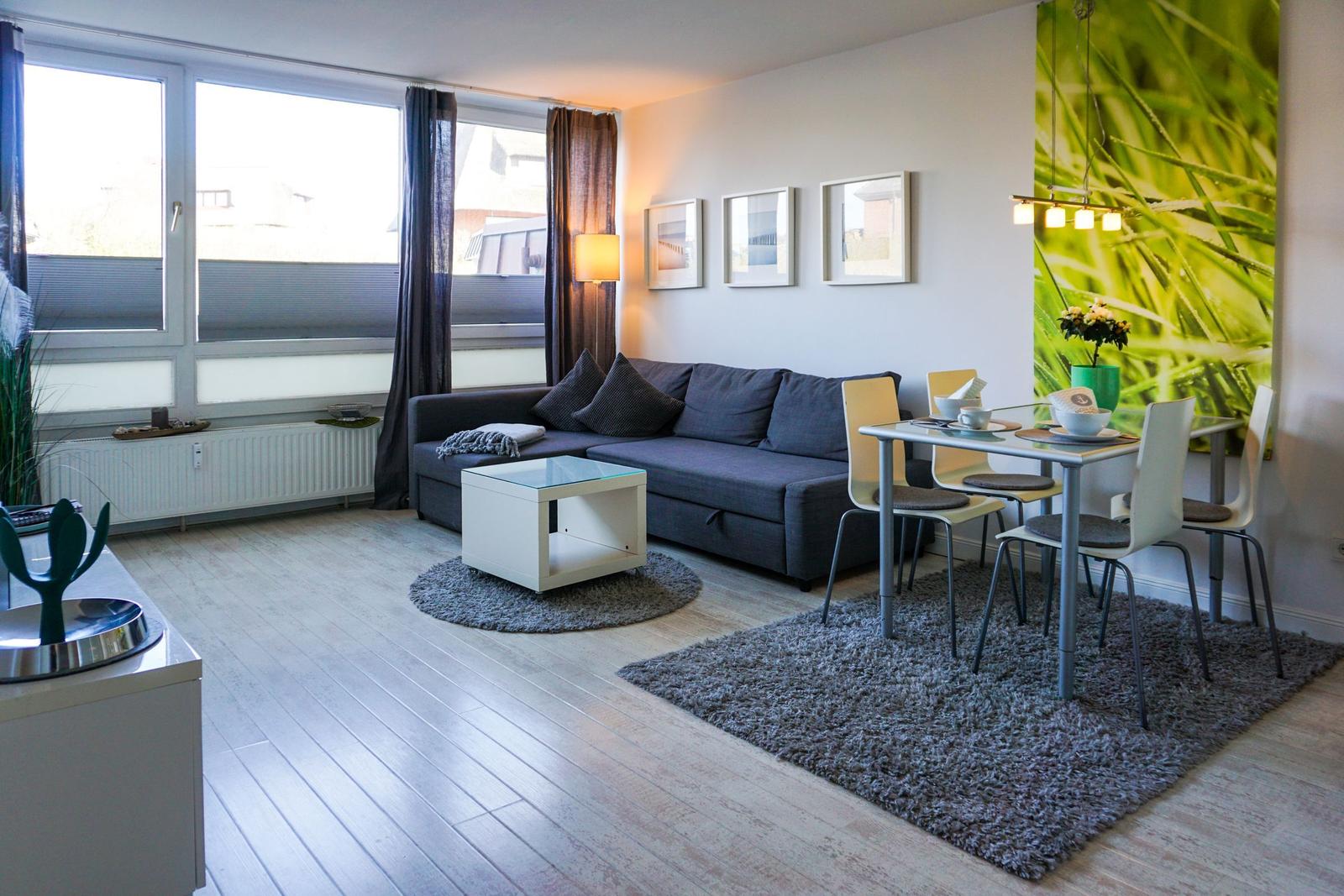 Wohn- und Essbereich mit Sofa, Tisch und Stühlen. Große Fenster und Wandbild.