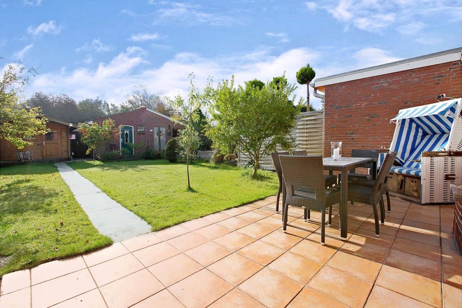 Terrace with table, chairs, and beach chair. Lawn and garden path in background.