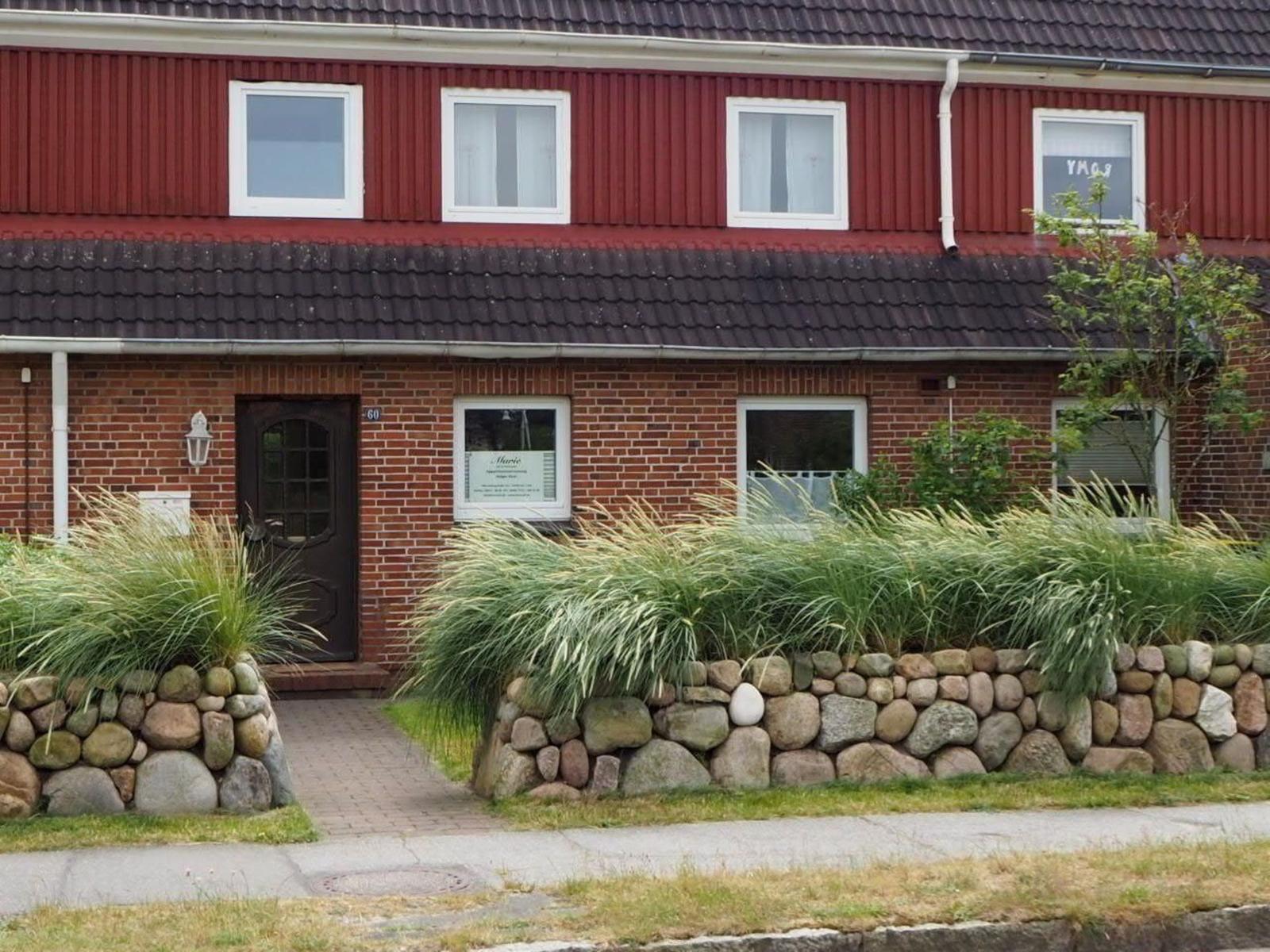 Red wooden house with stone wall and greenery