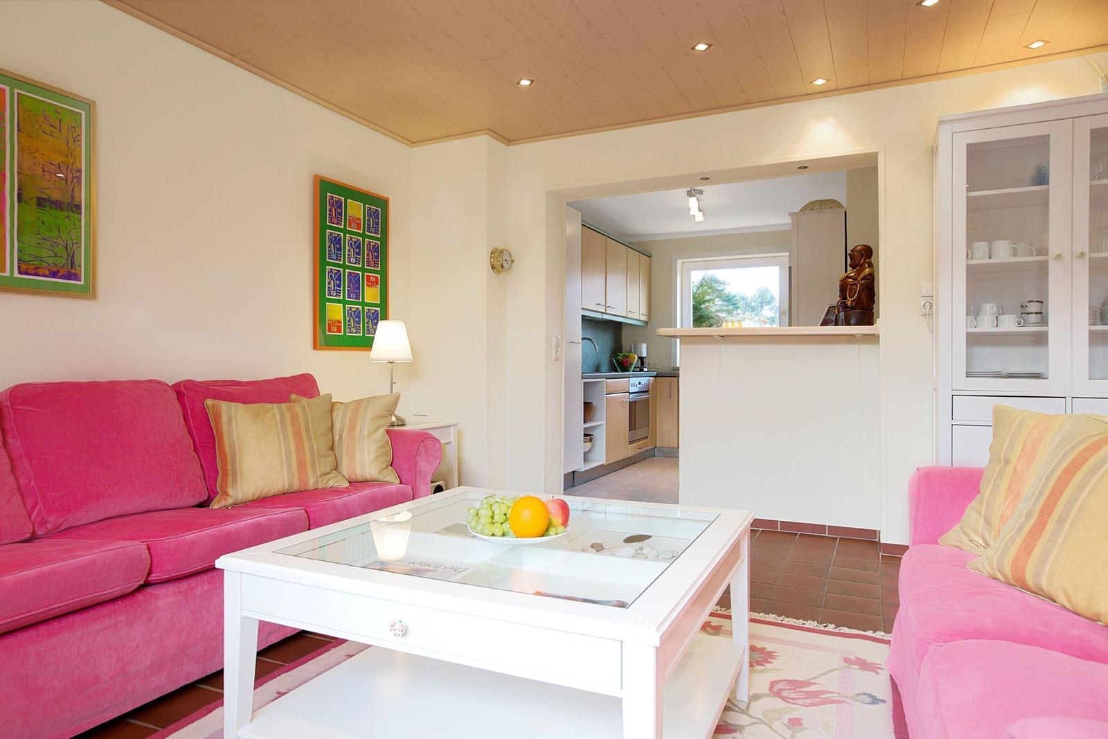 Living area with pink sofas, glass table, and view into the kitchen.