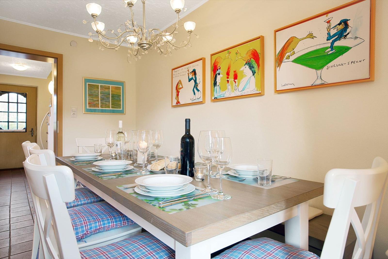 Dining table with white chairs and plaid cushions. Wall art and chandelier.