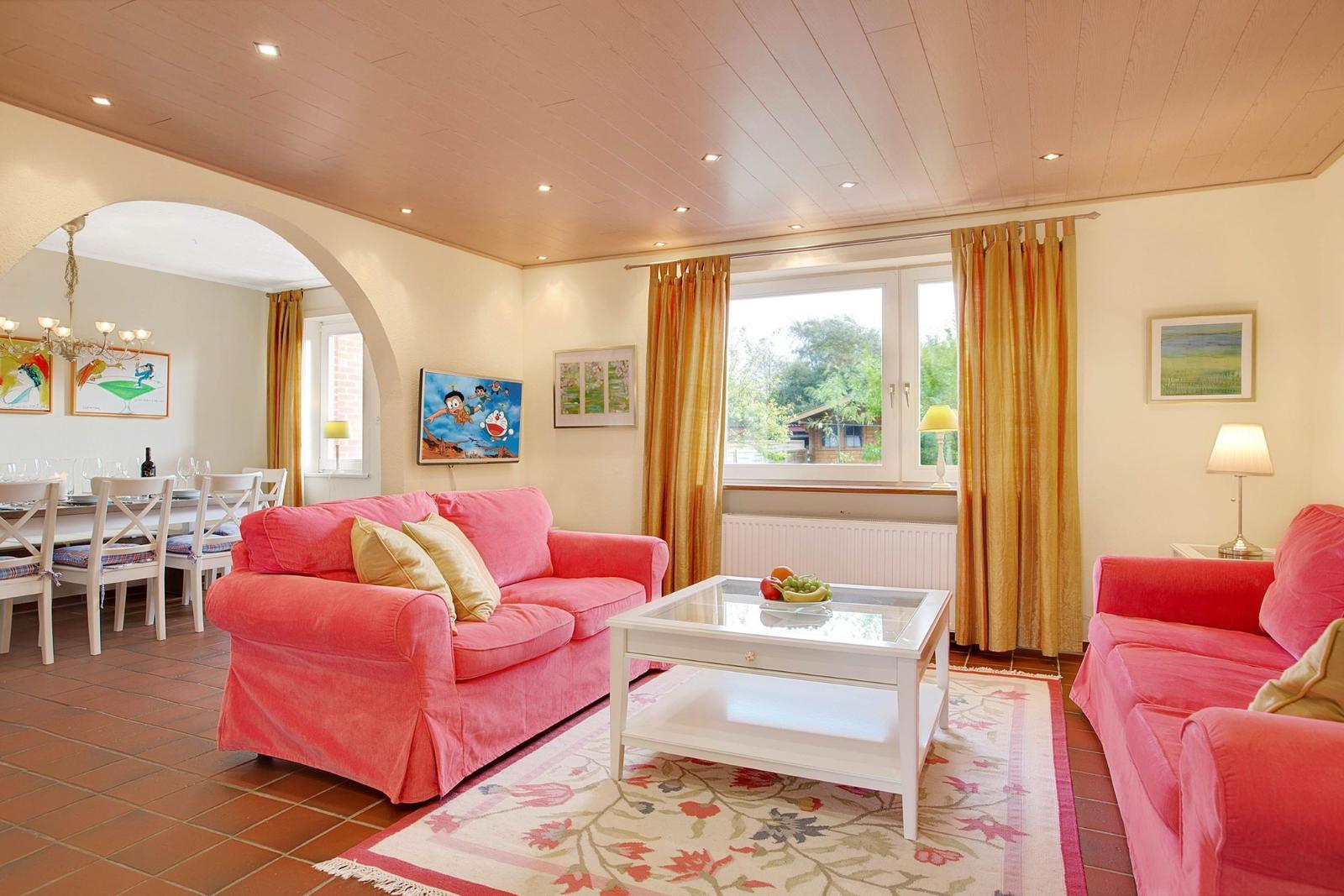Living room with pink sofas, glass table, and garden view.