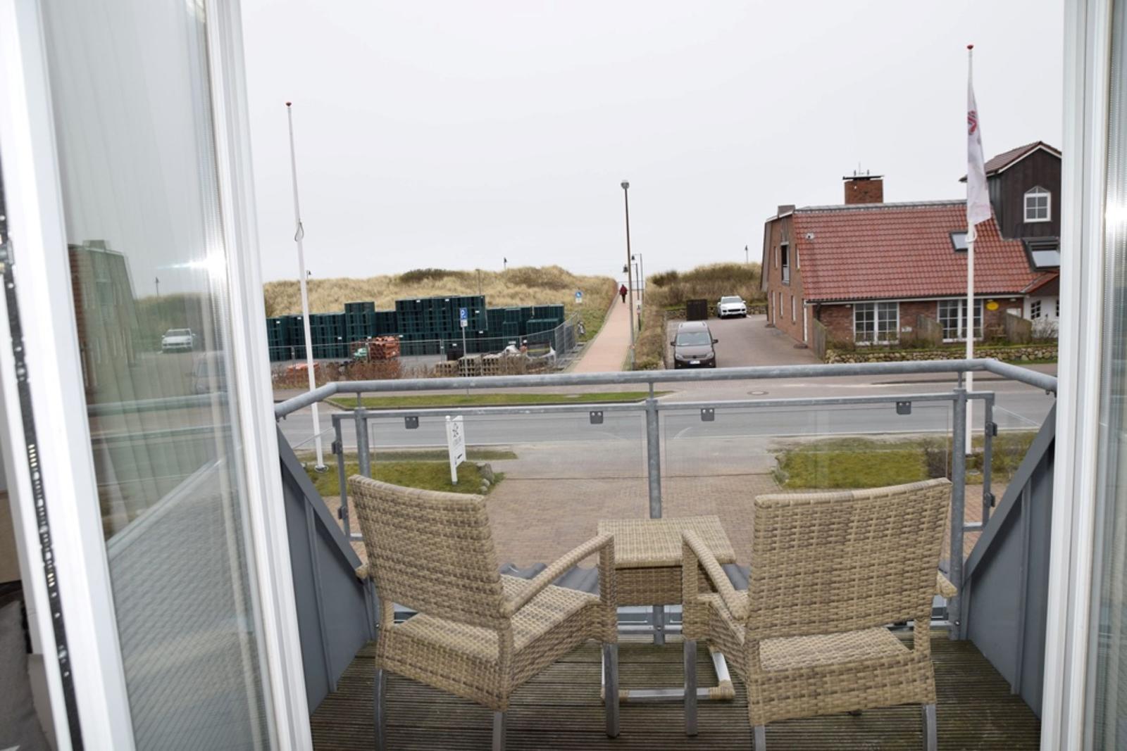 Balcony with two wicker chairs and table overlooking street and houses.