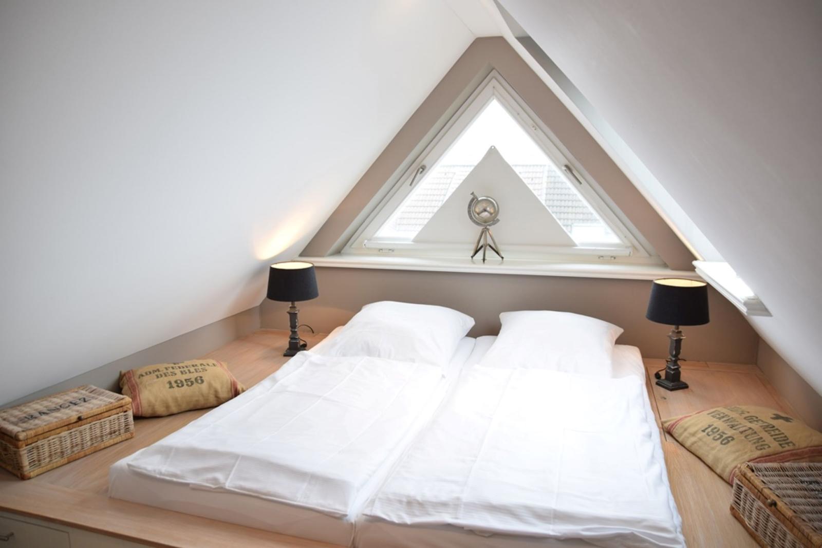 Schlafzimmer mit Dachschrägen, Doppelbett, zwei Nachttischen und einem Dreiecksfenster.