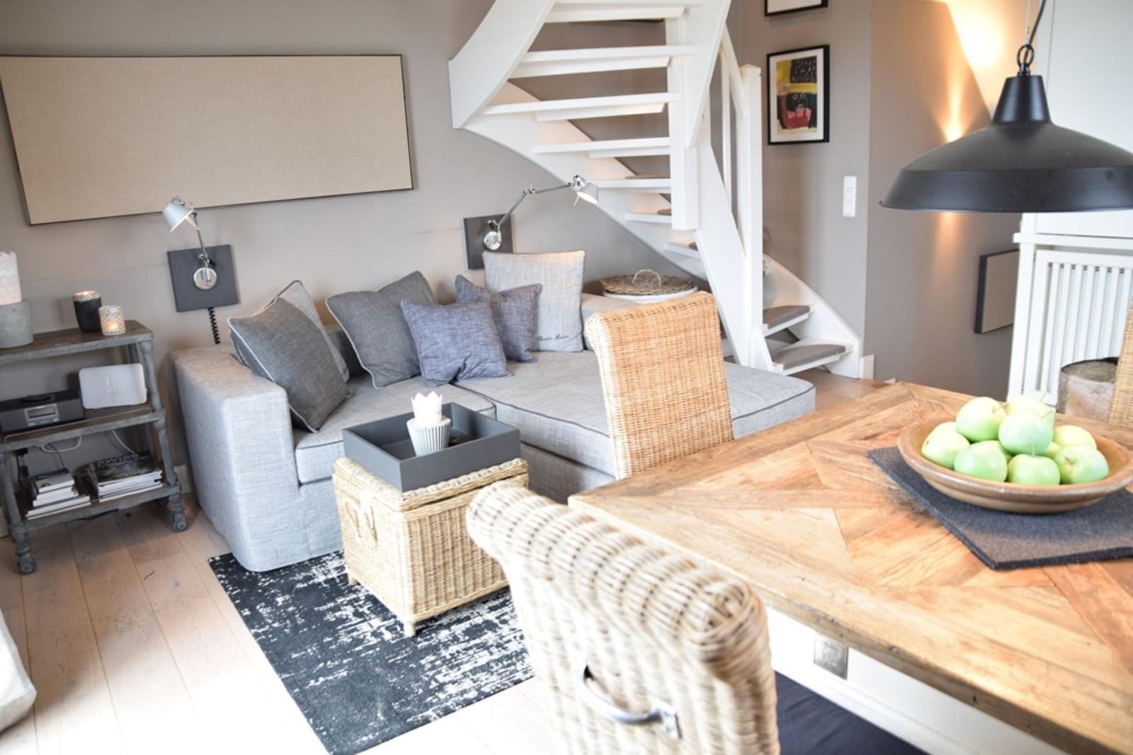 Wohn- und Essbereich mit grauem Sofa, Holztisch und Wendeltreppe.