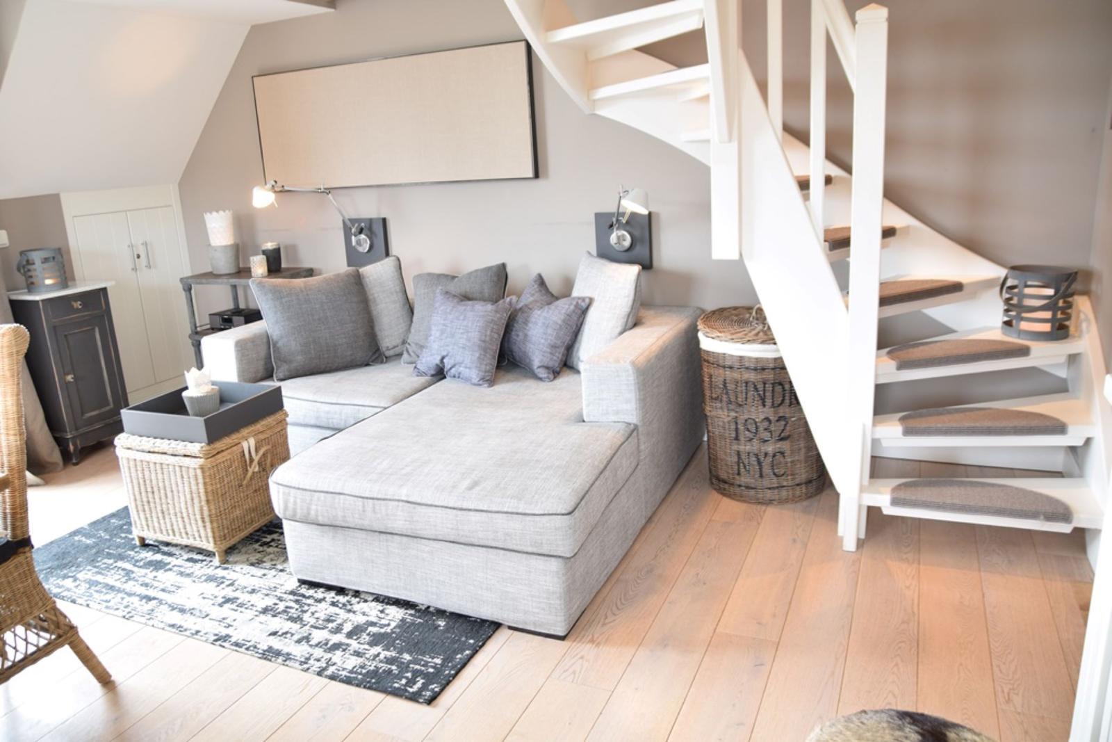 Wohnzimmer mit grauem Sofa, Holzboden und Wendeltreppe.