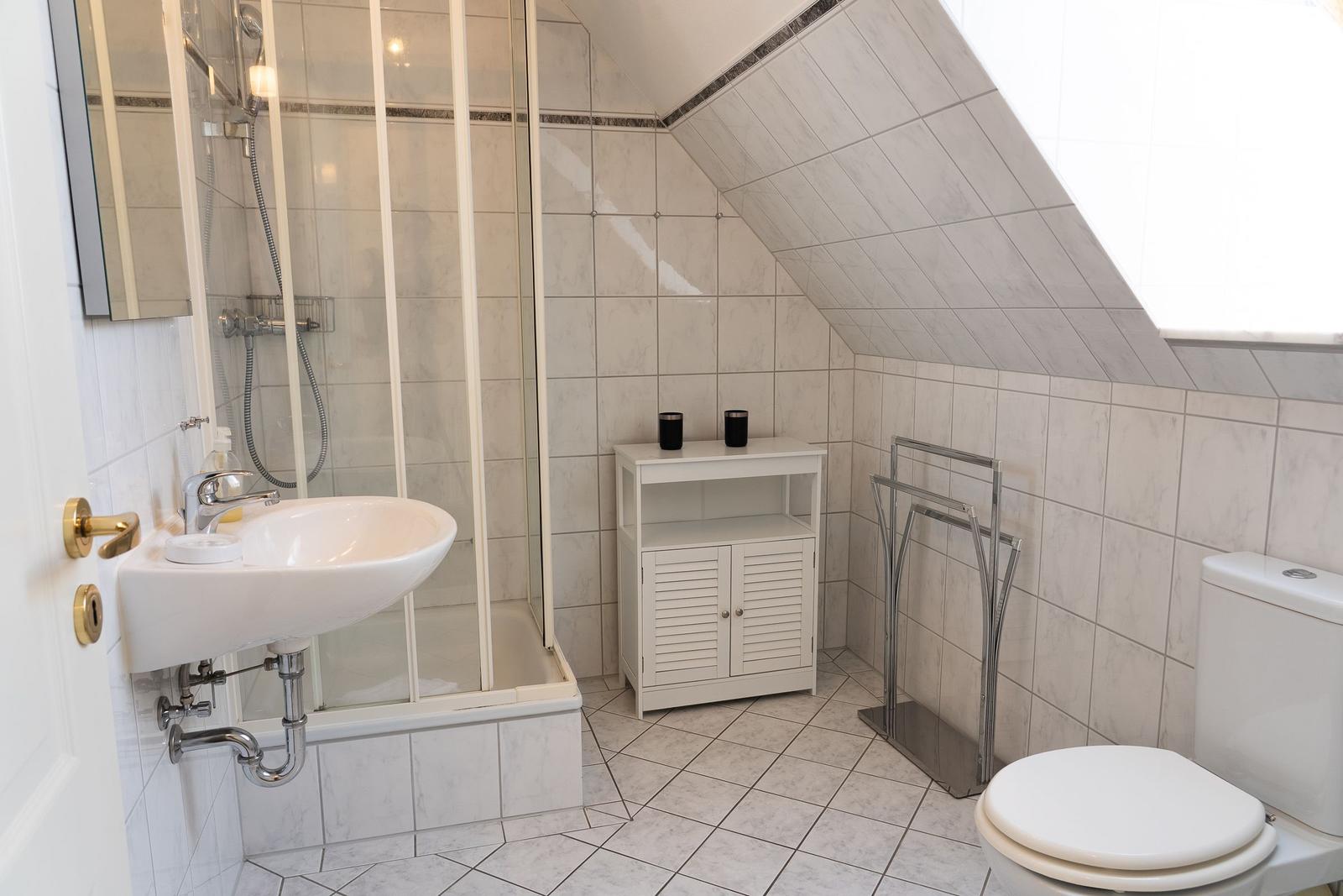 Badezimmer mit Dusche, Waschbecken und Toilette unter schräger Decke.