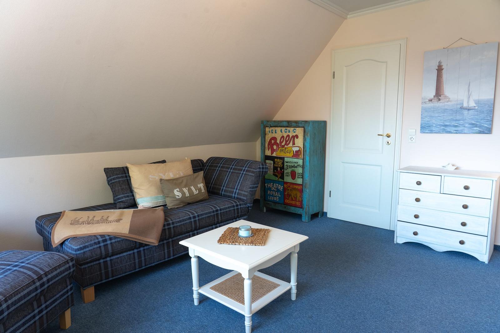 Schlafzimmer mit Sofa, Couchtisch und Kleiderschrank. An der Wand hängt ein Leuchtturm-Bild.